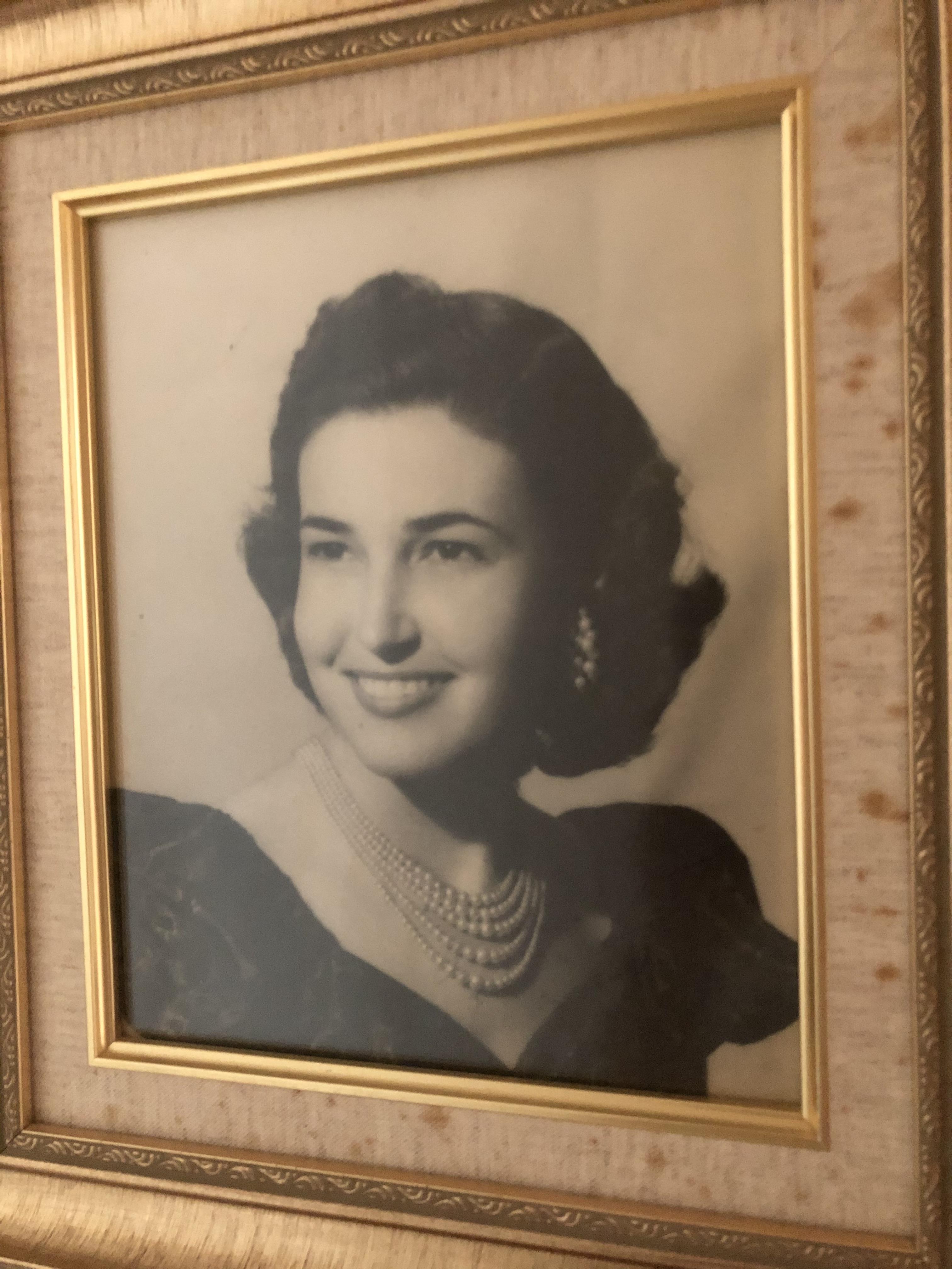 A classic portrait of a woman in a black dress and pearls, smiling warmly.