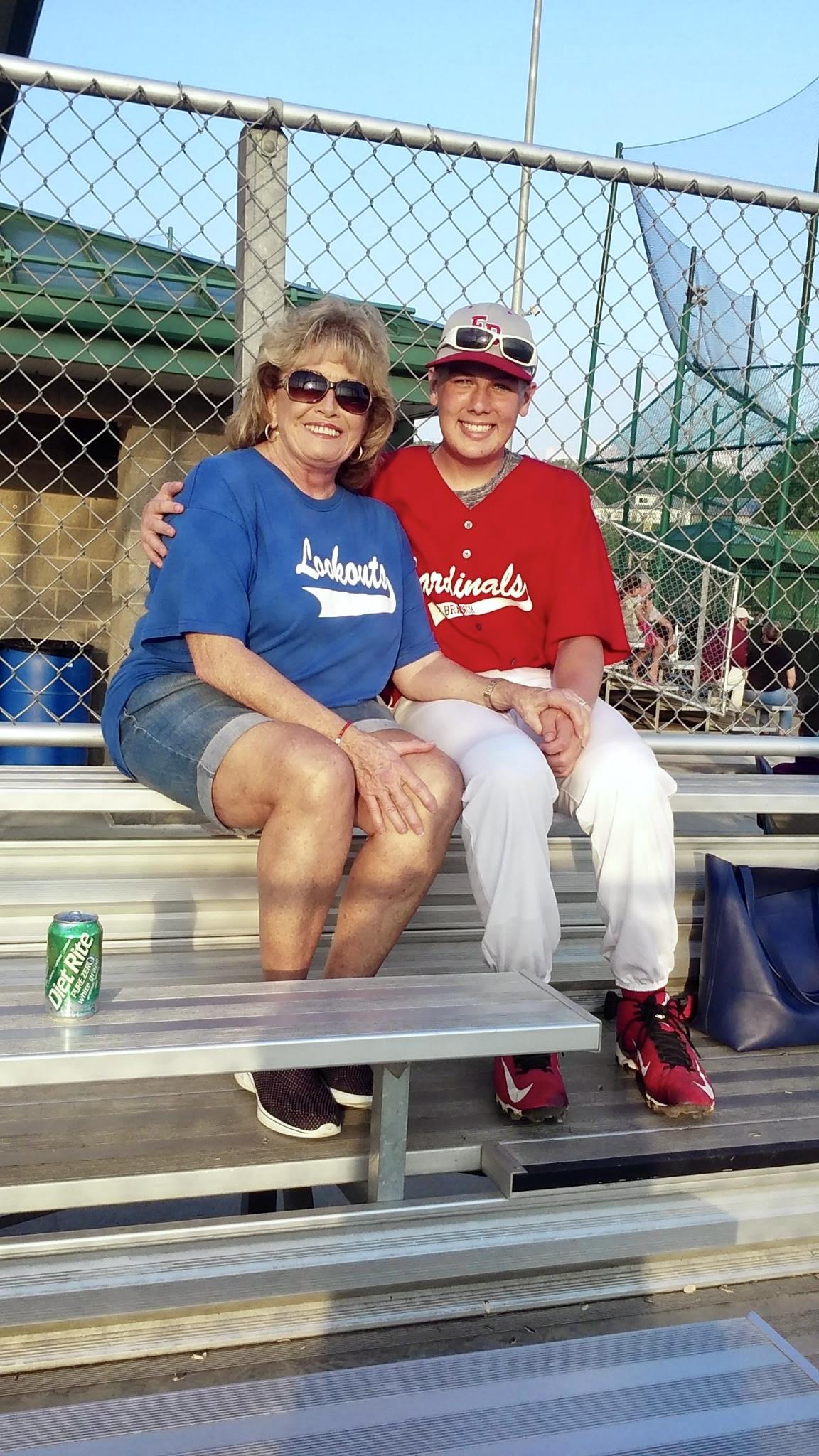 Two fans sit together wearing team jerseys and enjoying a baseball game on a warm day.