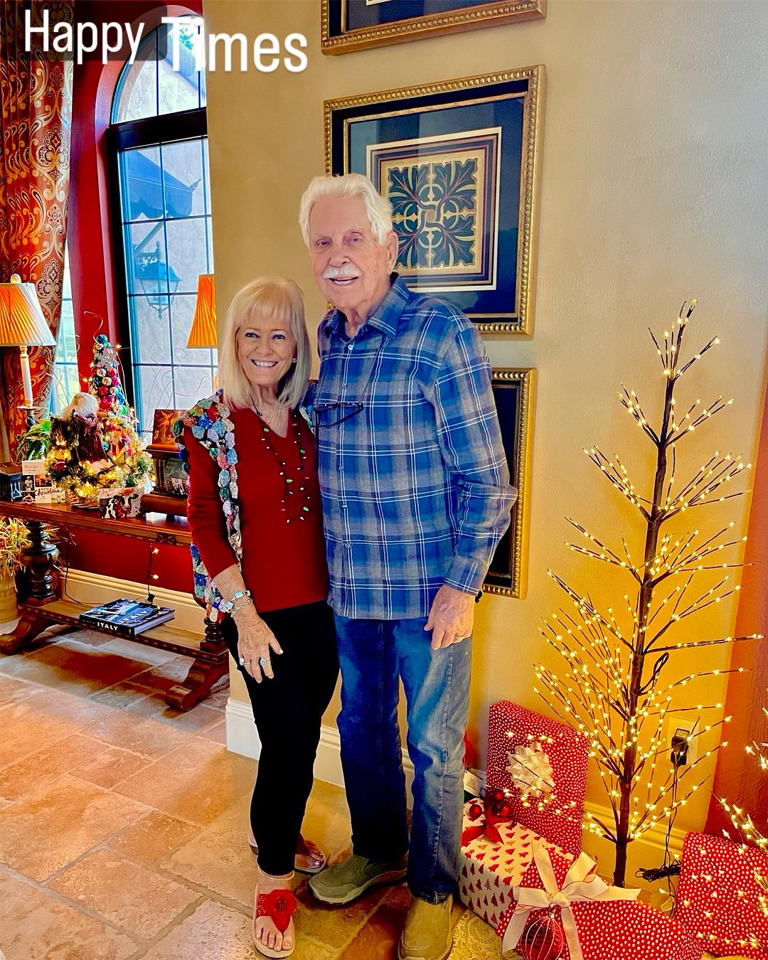 A cheerful couple stands together in a festive living room surrounded by holiday decorations.