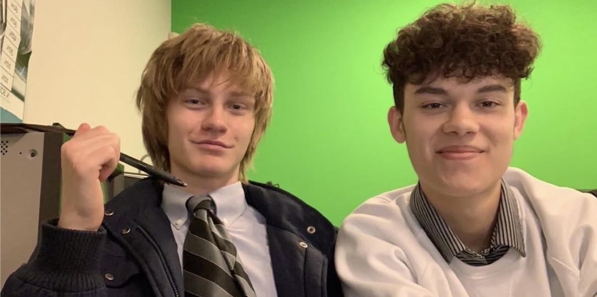 Two boys dressed smartly smile together against a vivid green backdrop during a casual moment.