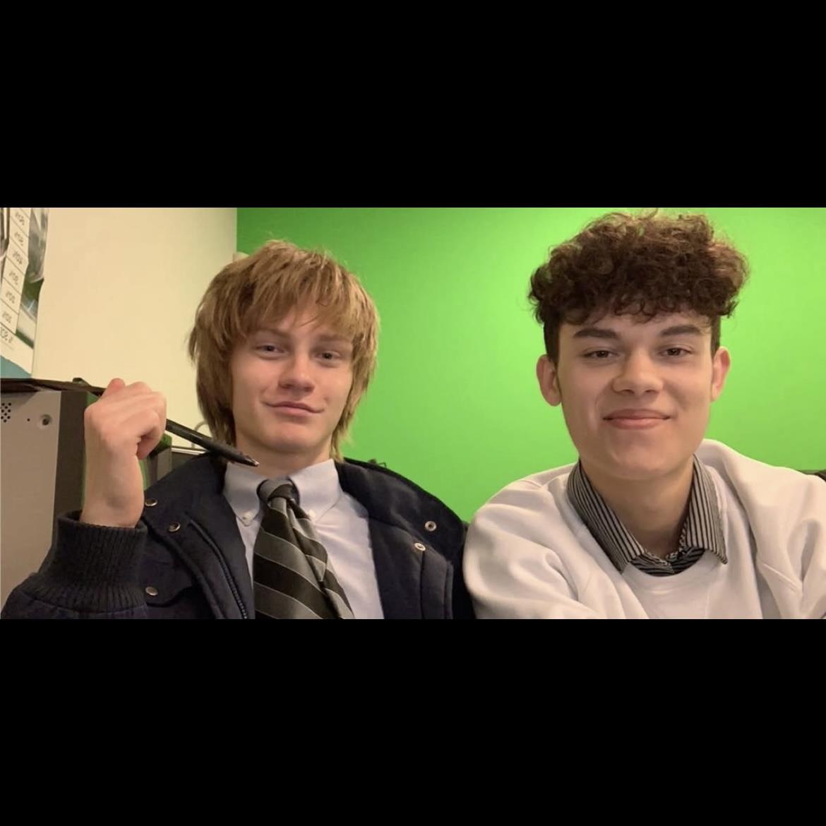 Two young boys relax and pose for a fun photo in a classroom setting with bright green screen.