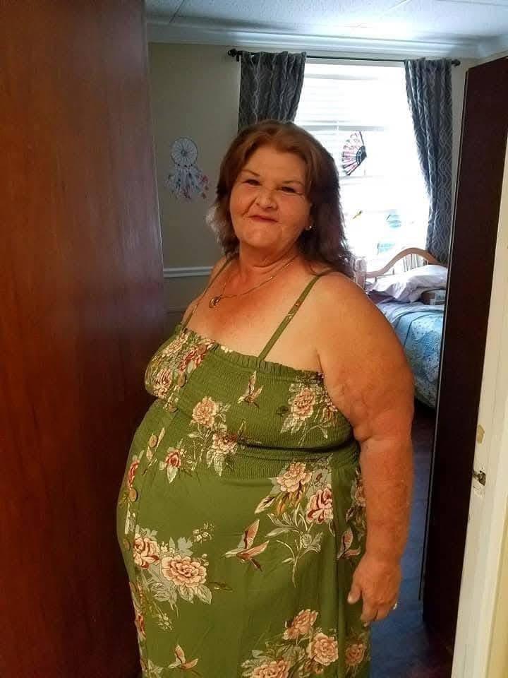 A woman in a floral dress stands in a doorway, smiling in natural light.