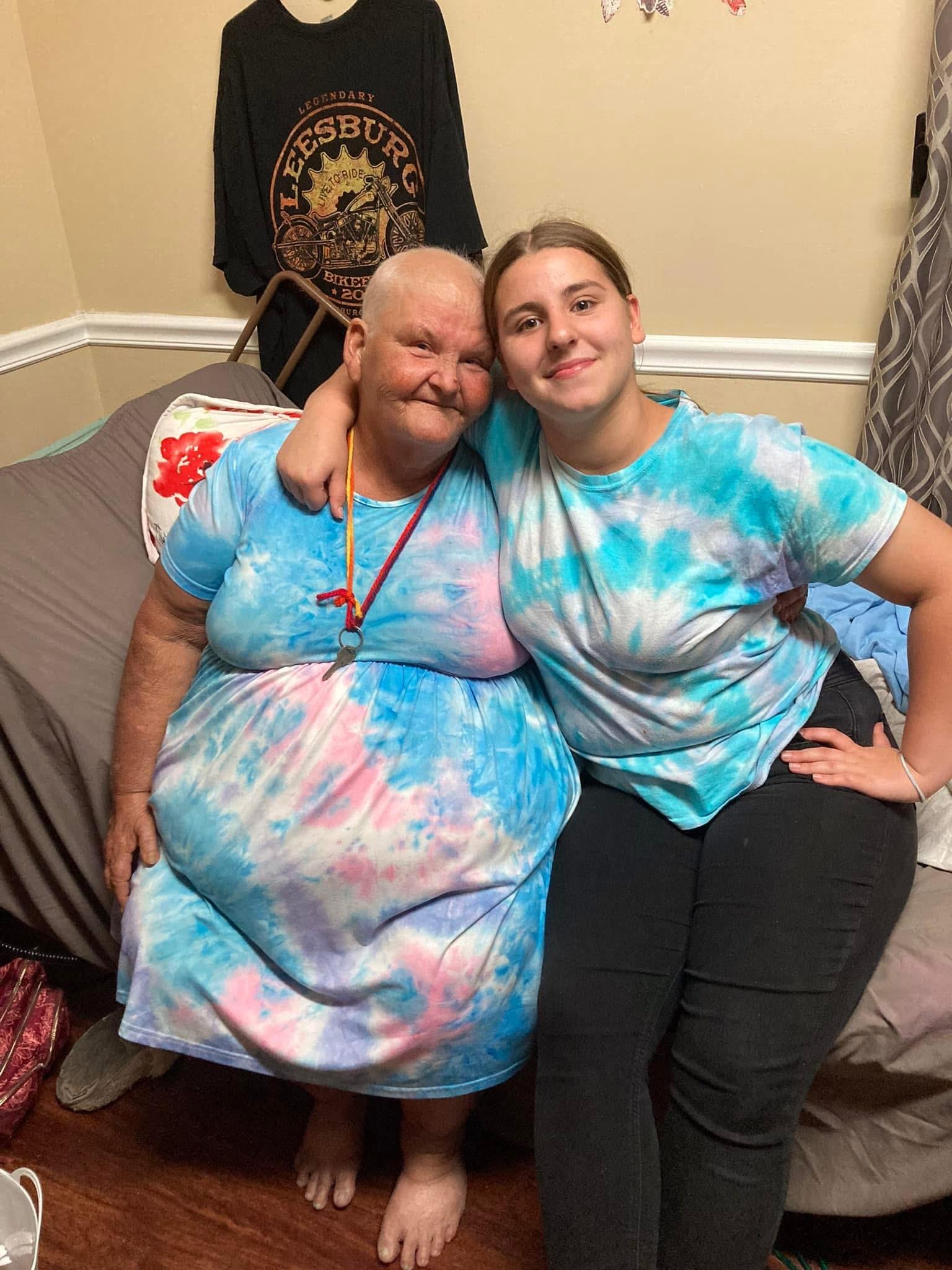 Two family members sit together on a couch, both wearing colorful tie-dye clothing and smiling.