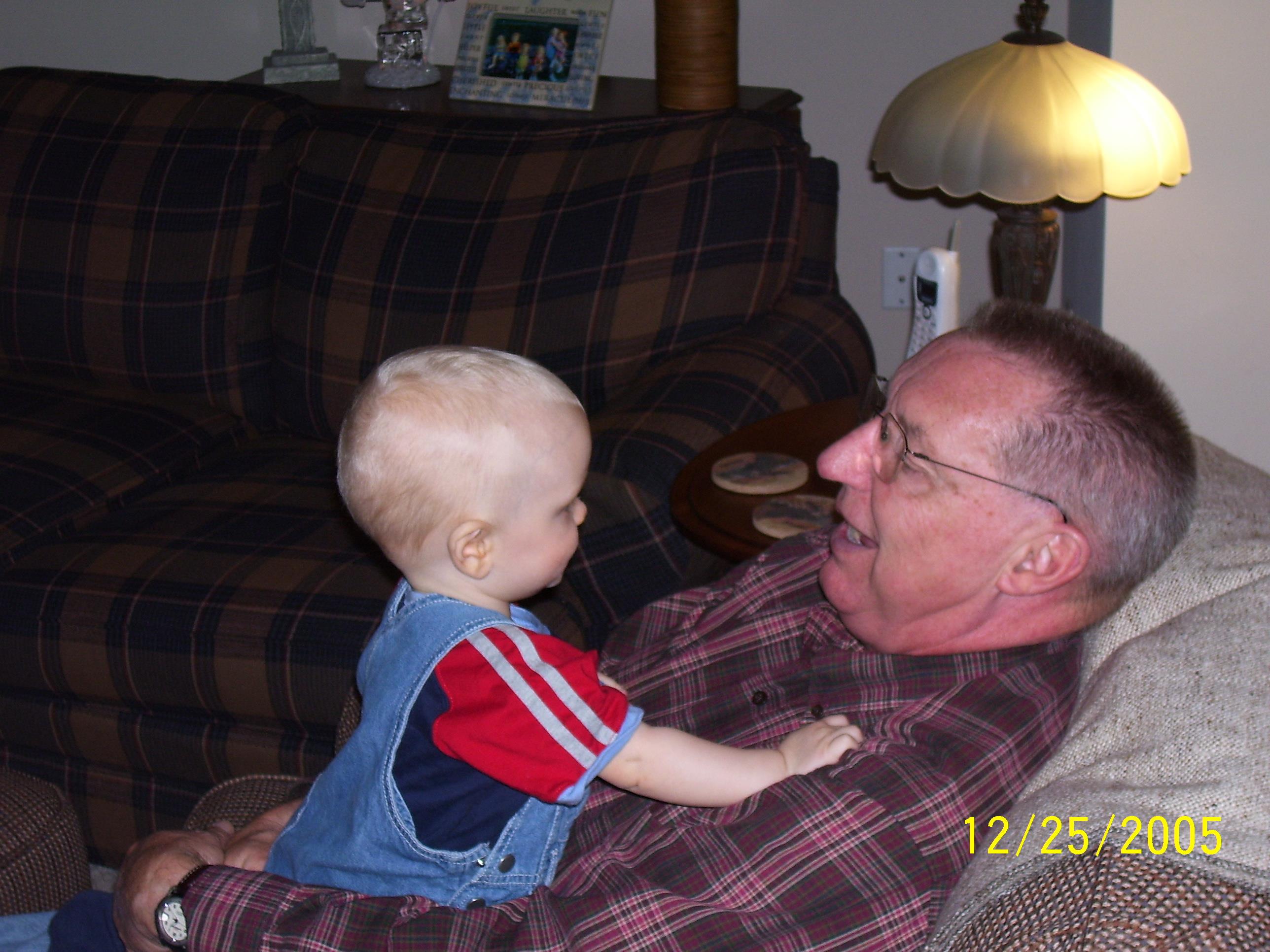 A toddler shares a joyful interaction with a grandfather on a cozy couch during a family gathering.