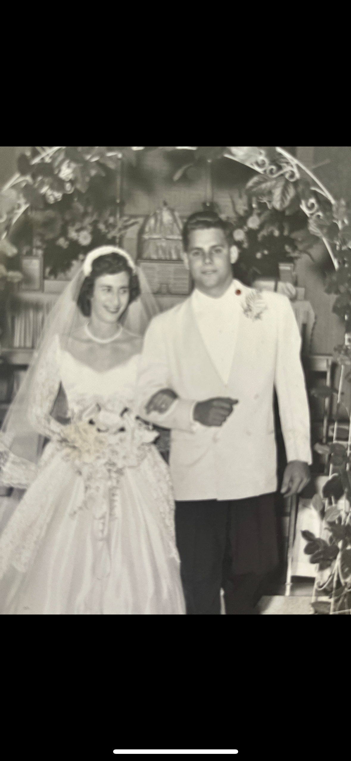 A newlywed couple walks together, smiling happily in a decorated setting with flowers.