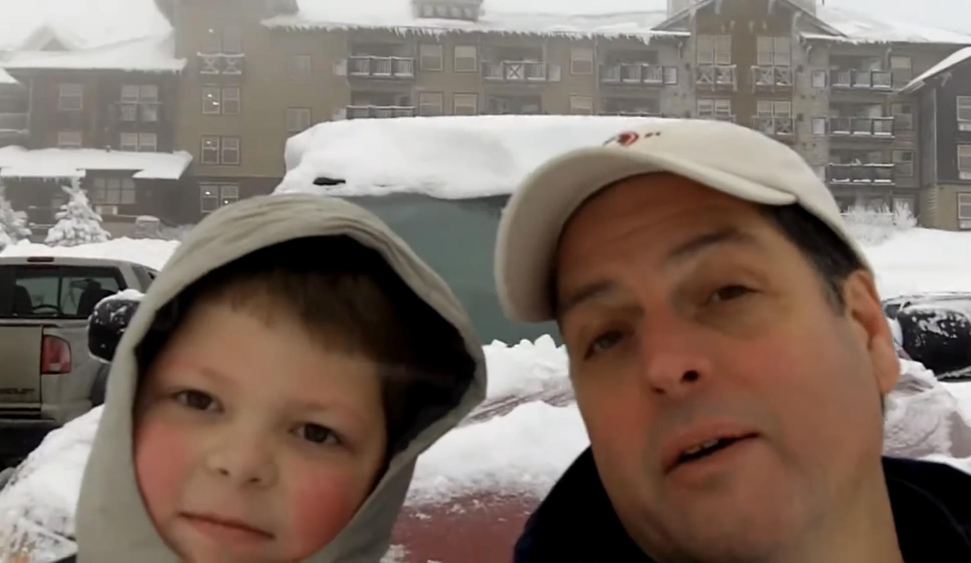 Father and son smile together while surrounded by snow in a winter setting.