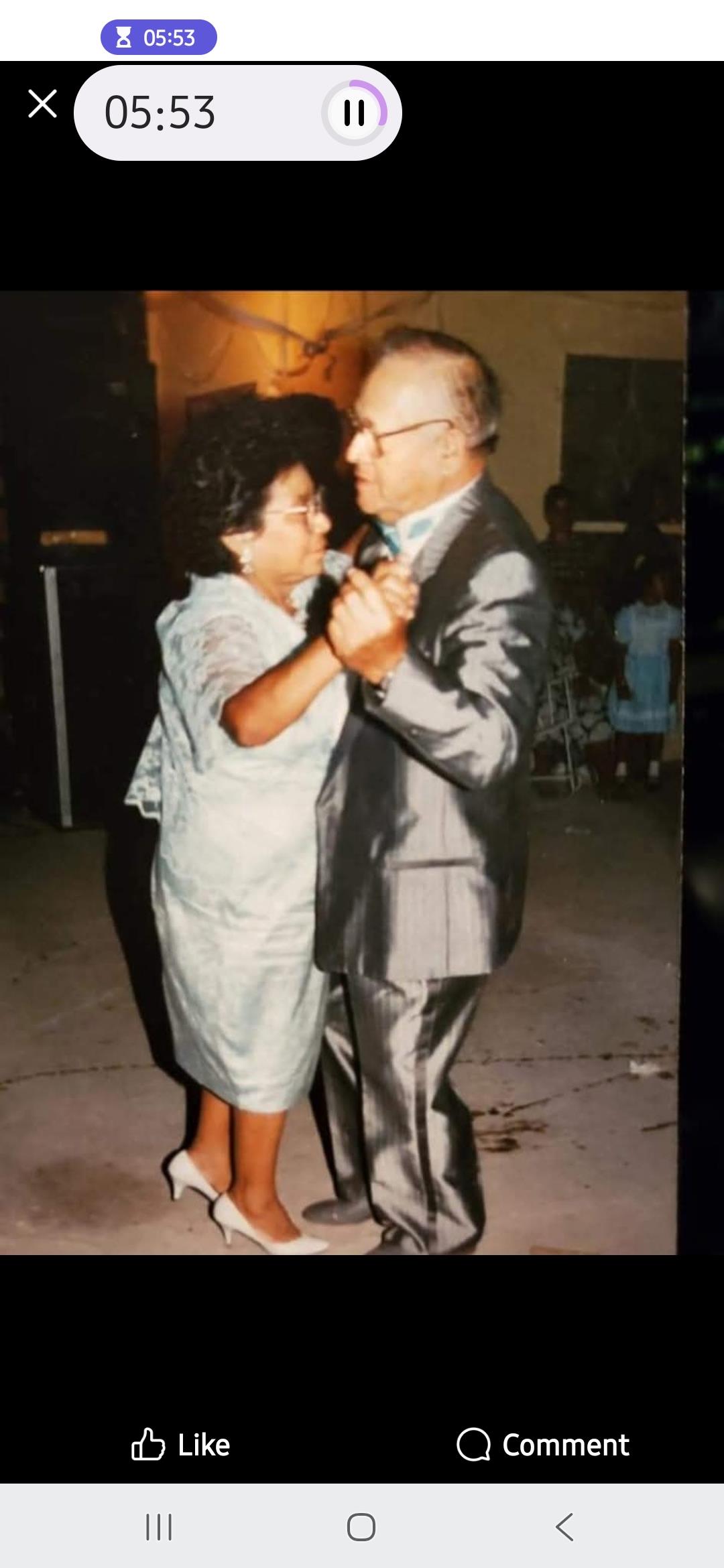 Elderly couple shares a loving dance in formal attire at a social gathering in the evening.