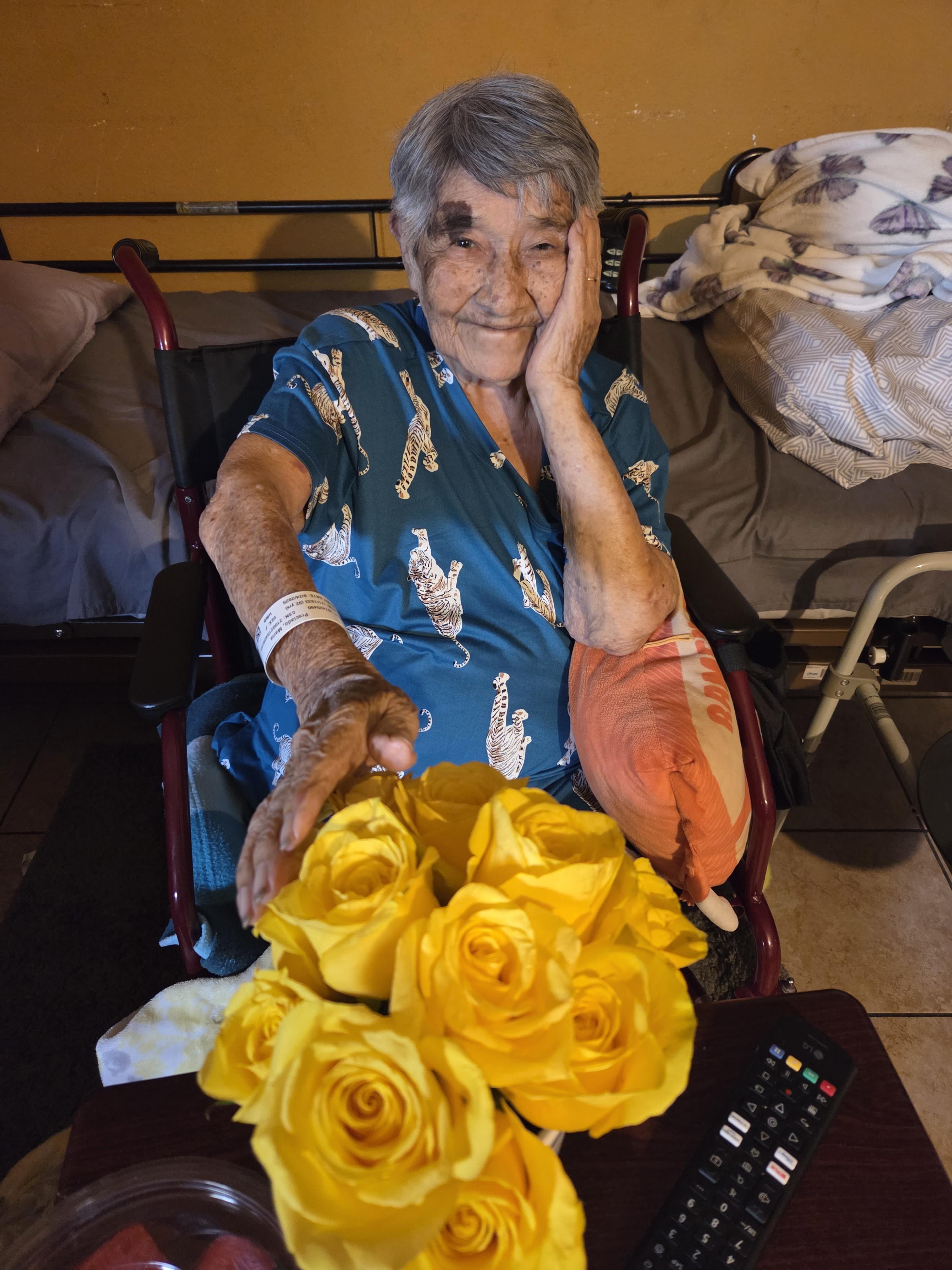 A senior woman enjoys a moment with yellow roses, smiling as she recalls happy memories.