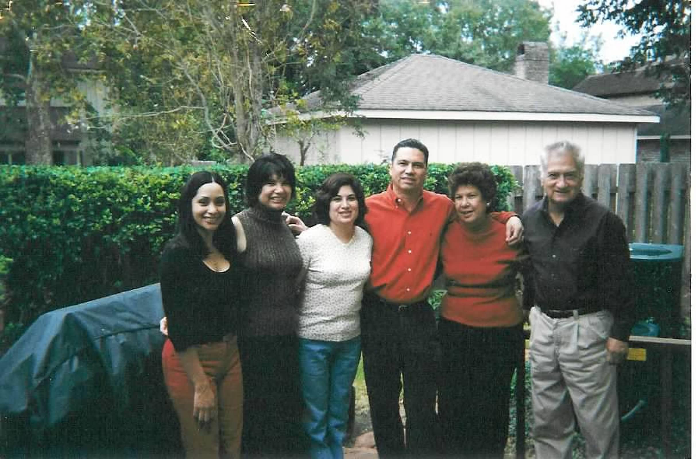Friends and family stand together, smiling and enjoying their time in a backyard setting.