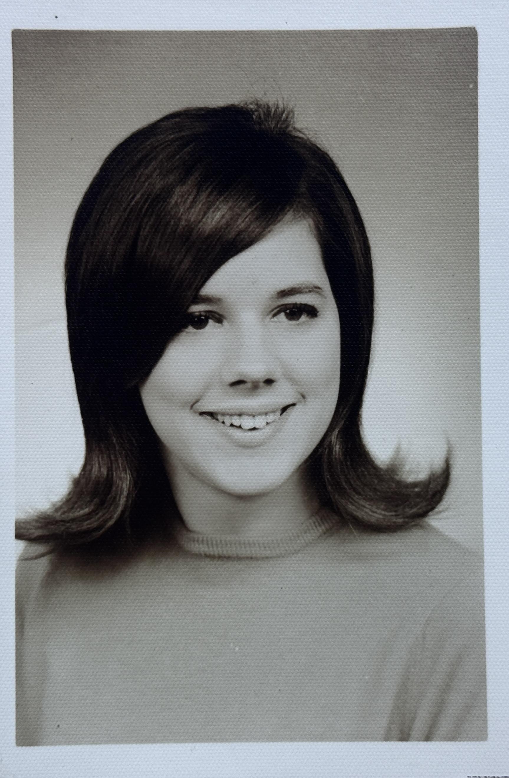 A cheerful young woman poses with a bright smile and 1970s hairstyle in a studio portrait.