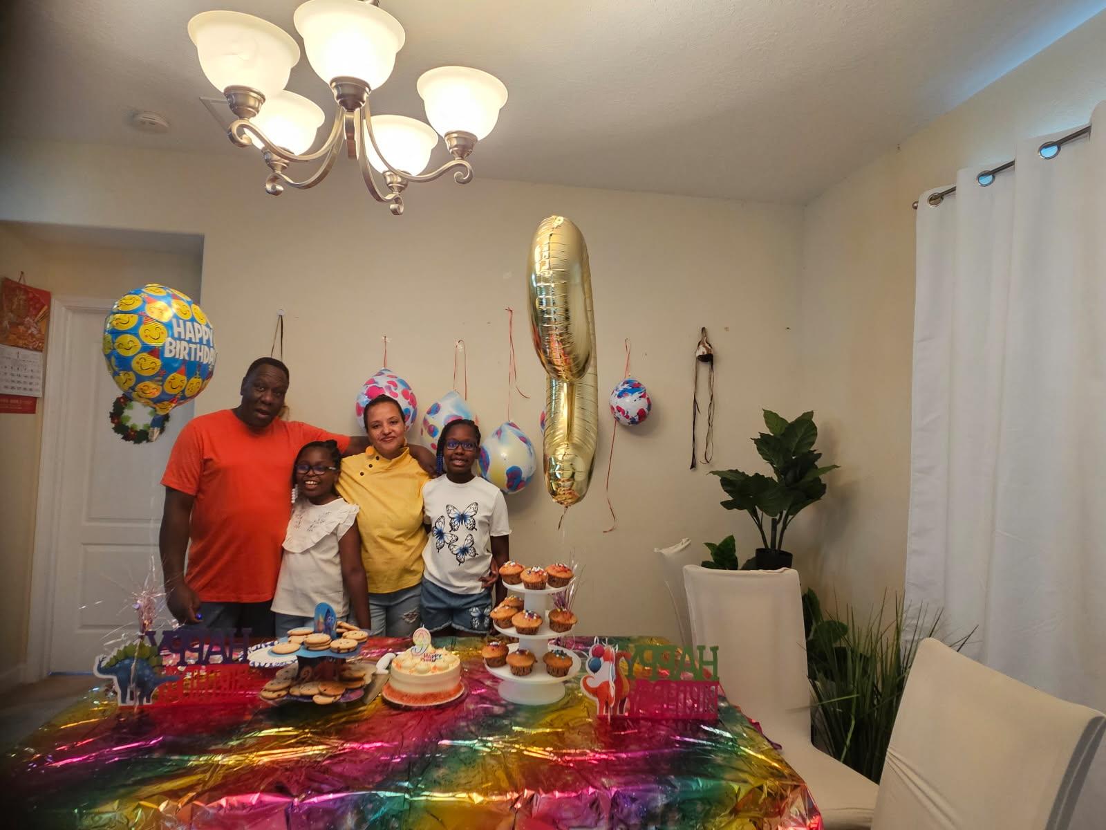 Family stands together with food and decorations during a birthday party in a home.
