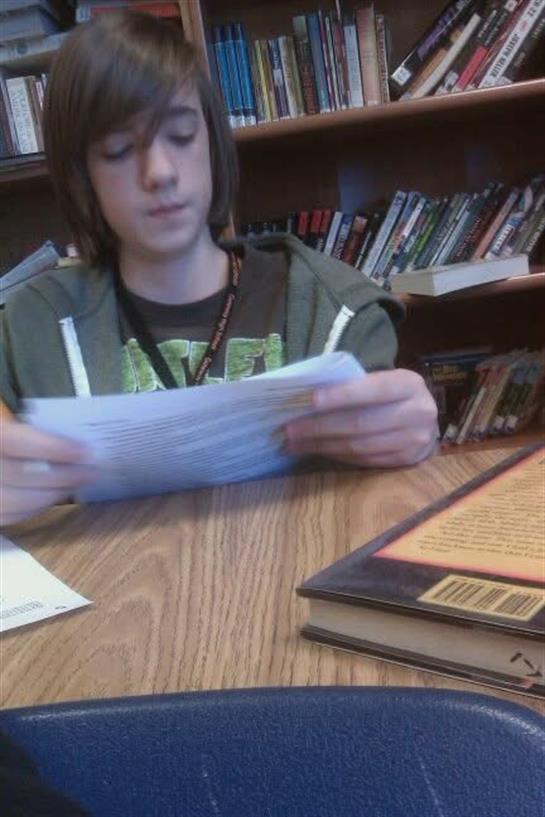 A boy sitting at a table reading a paper