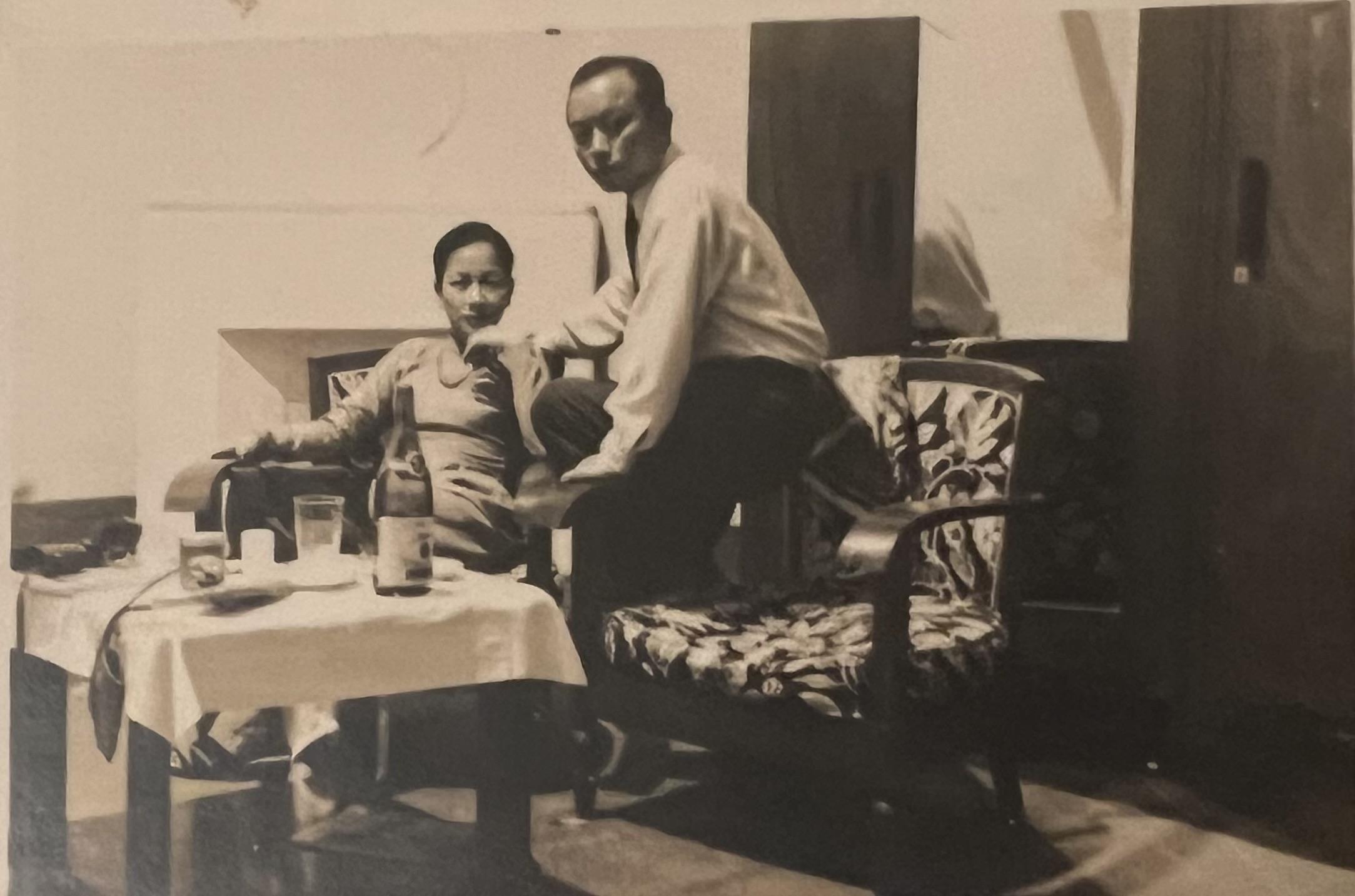 Two individuals are seated in a room, enjoying drinks on a table. They appear to be relaxed.