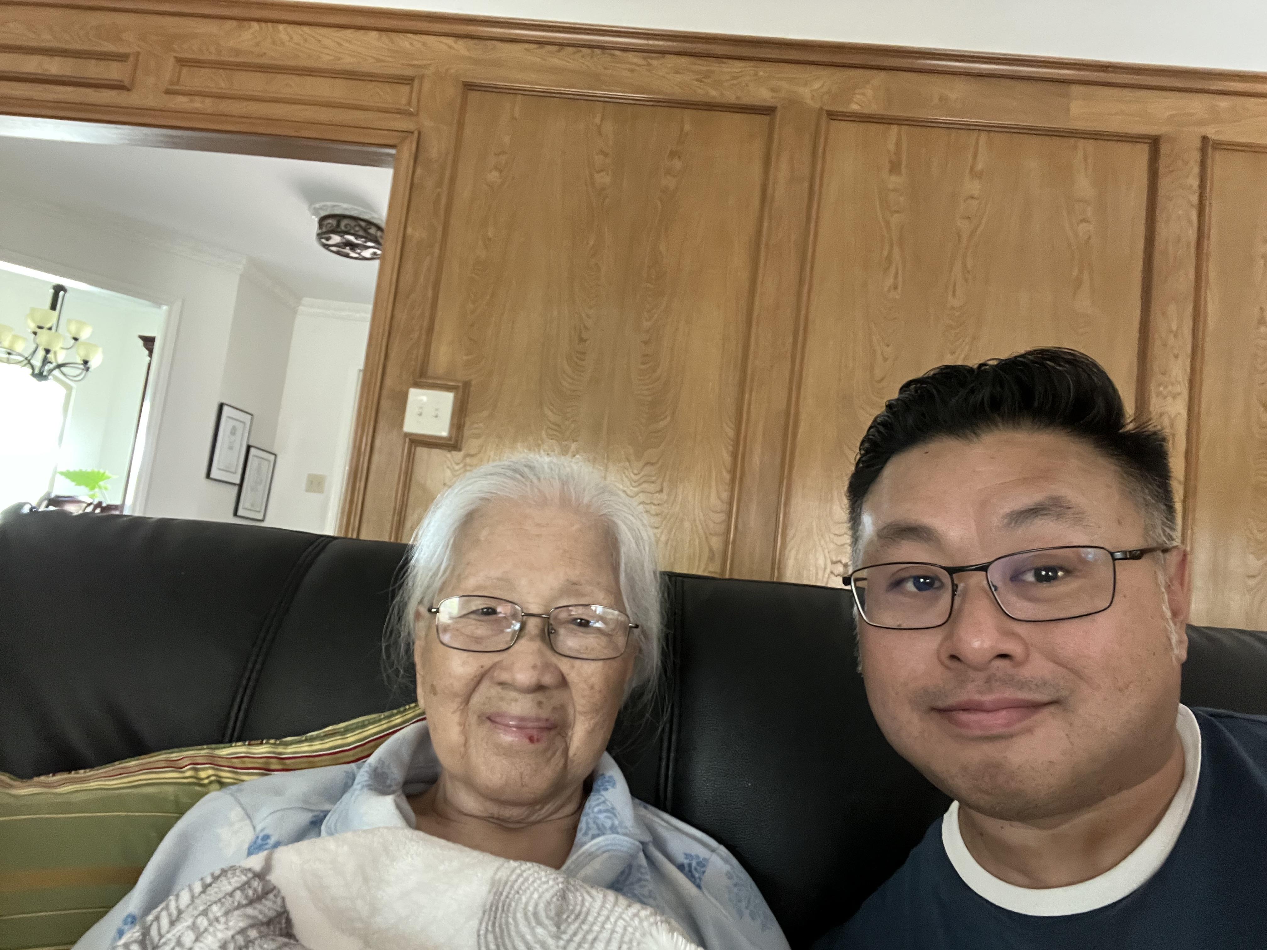 A man and an elderly woman sit together on a couch in a living room.