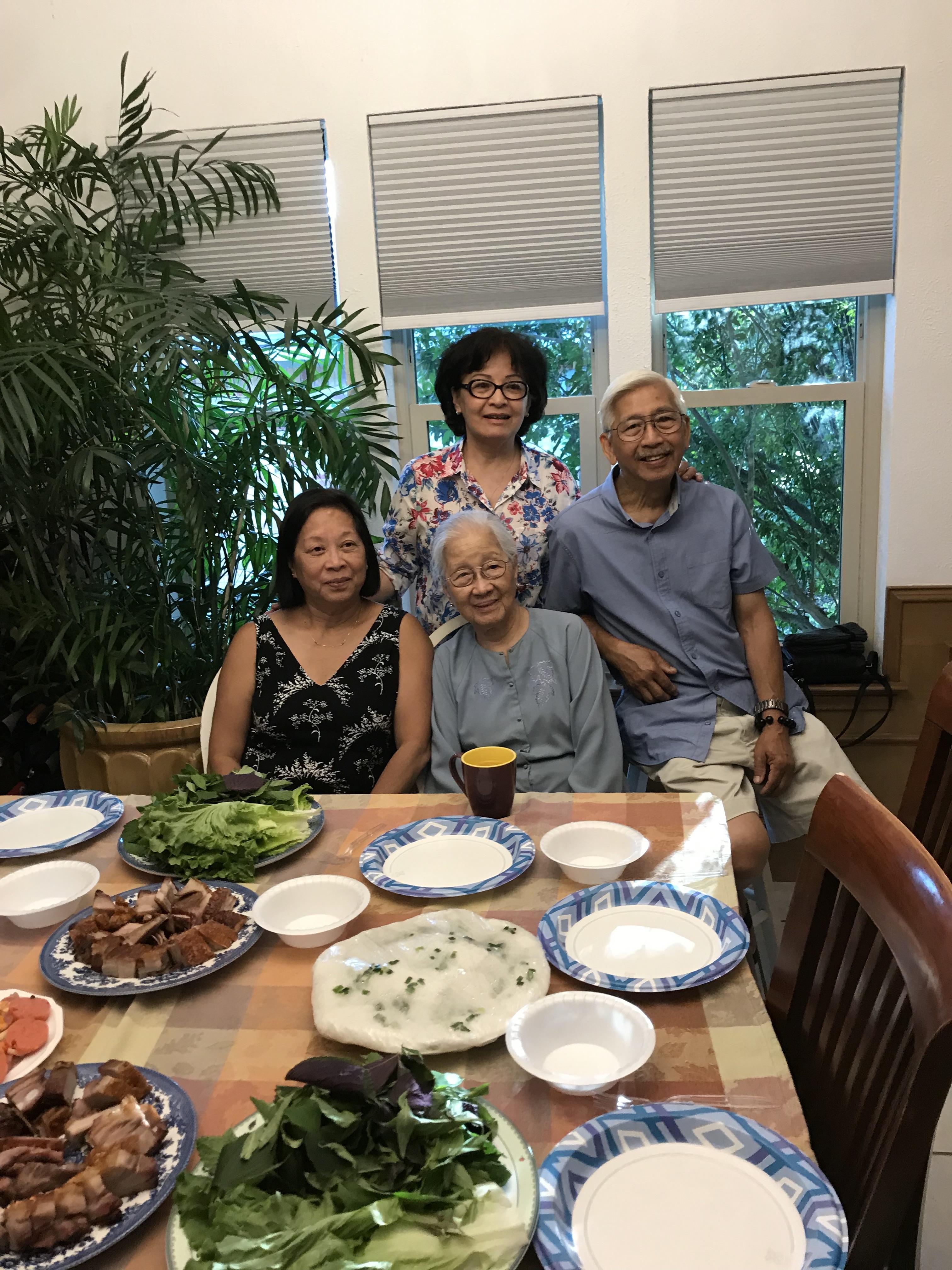Four family members enjoy food together at home during a sunny day with plenty of light.