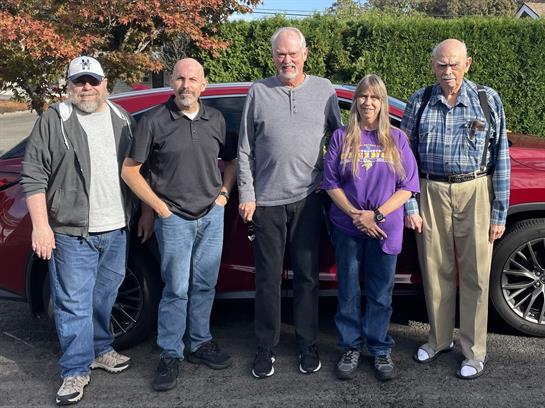 A group of people standing in front of a red car
