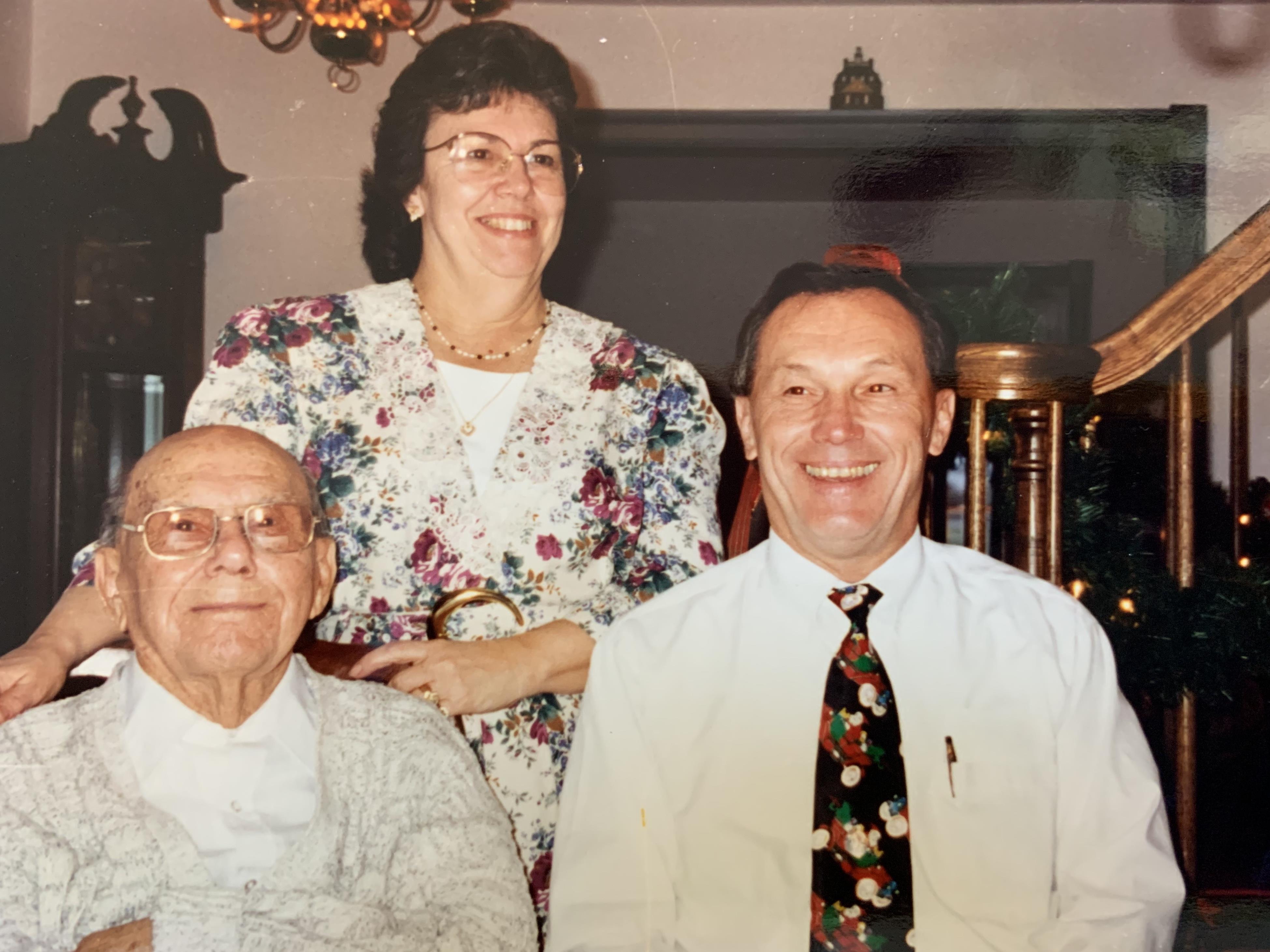 Three people stand and sit together, smiling at a gathering with warm lighting in the background.