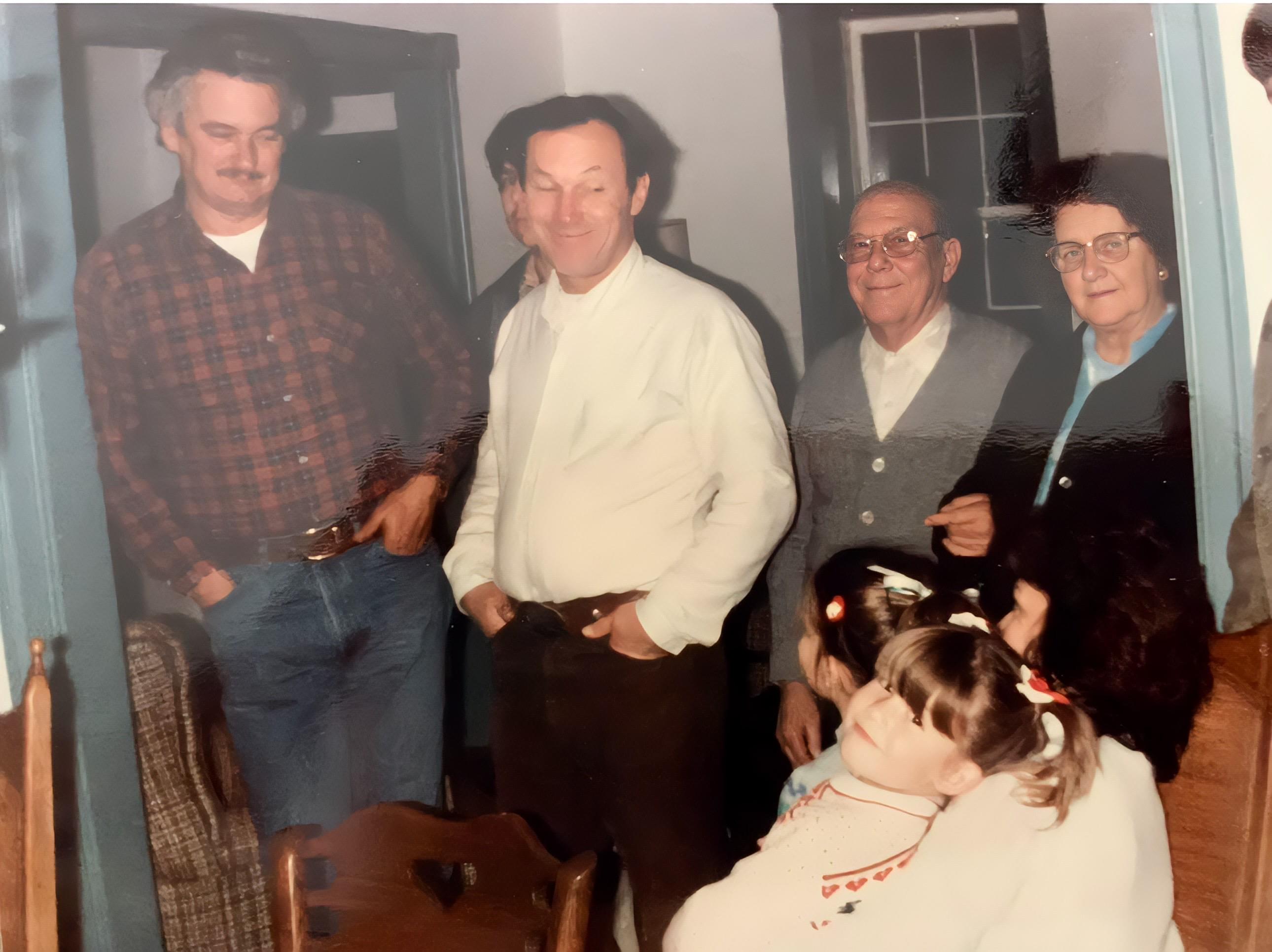 A group of men talk while children listen in a room filled with warmth and conversation.