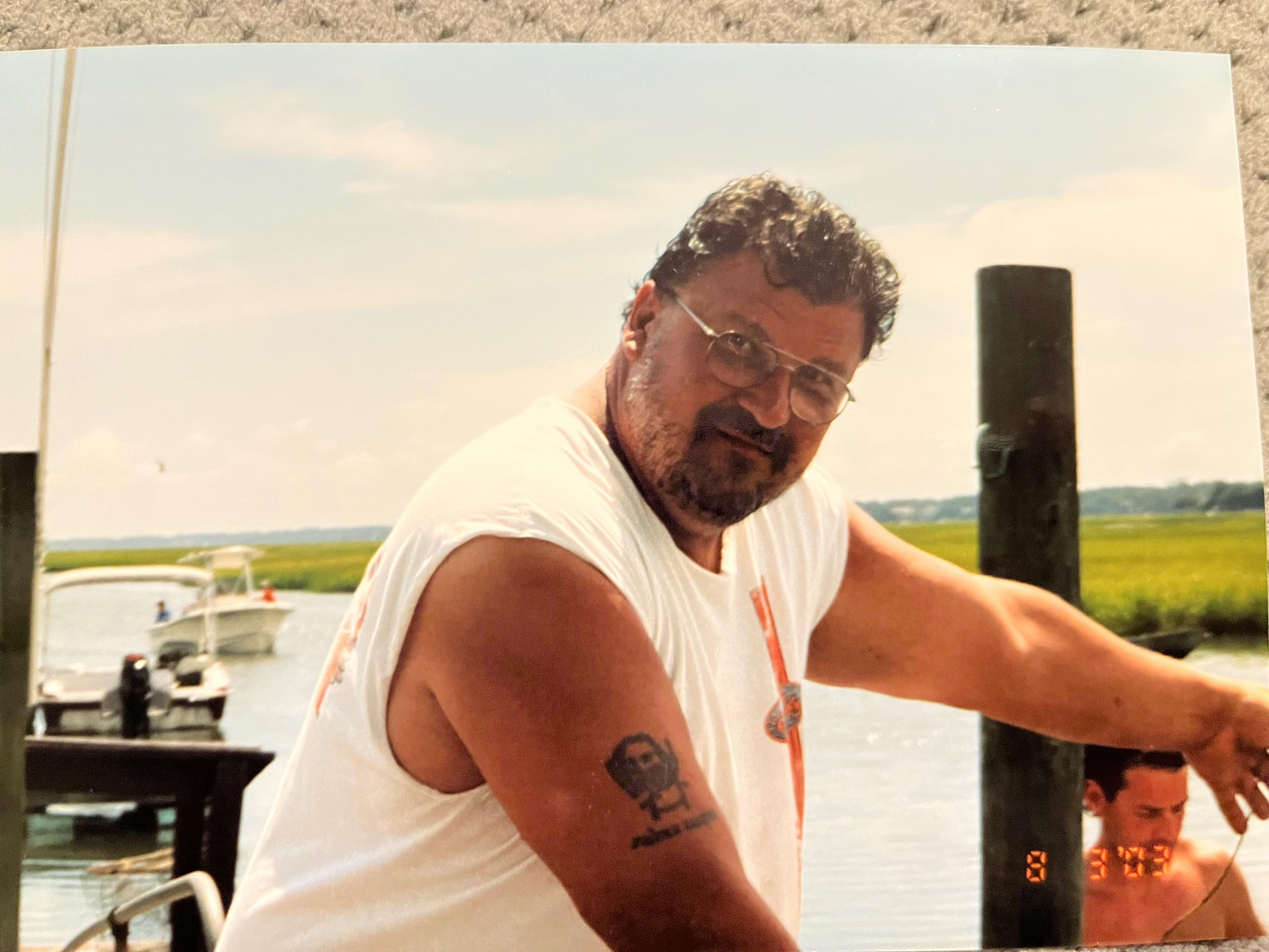 A man stands by the water at a dock, preparing for boating. Boats are moored nearby.