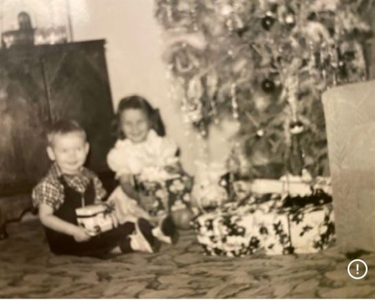 A boy and girl sitting next to a christmas tree