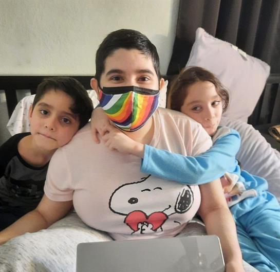 A group of children sitting on a bed with a woman wearing a face mask