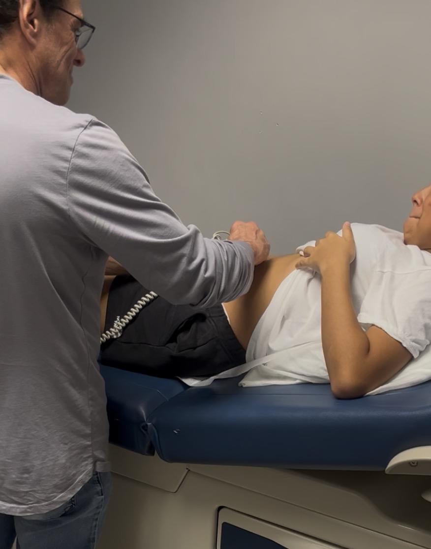 A doctor performs a check-up on a patient’s abdomen in a medical office.