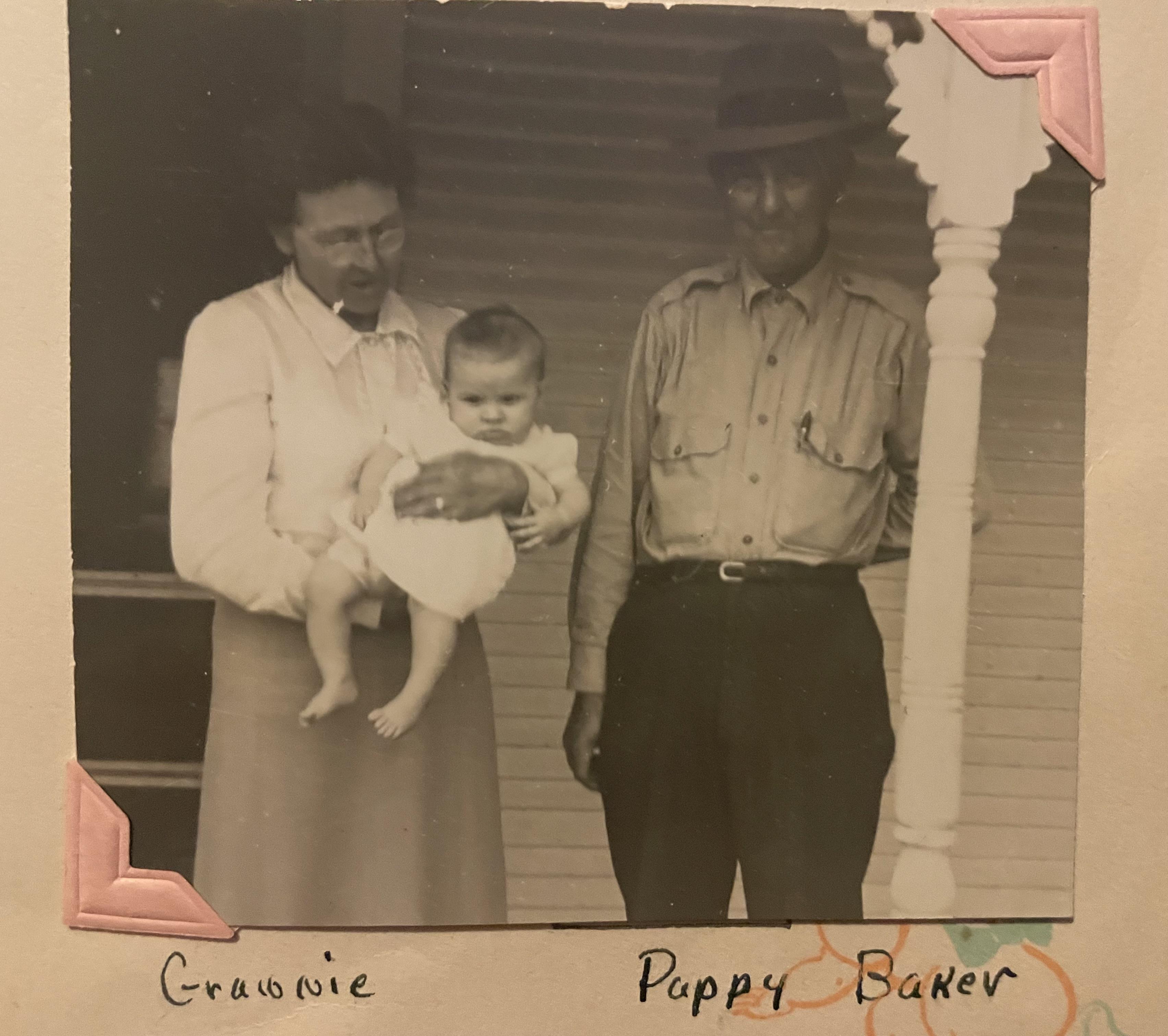 A man and woman hold a baby on a porch in a rural setting during the early 1900s.