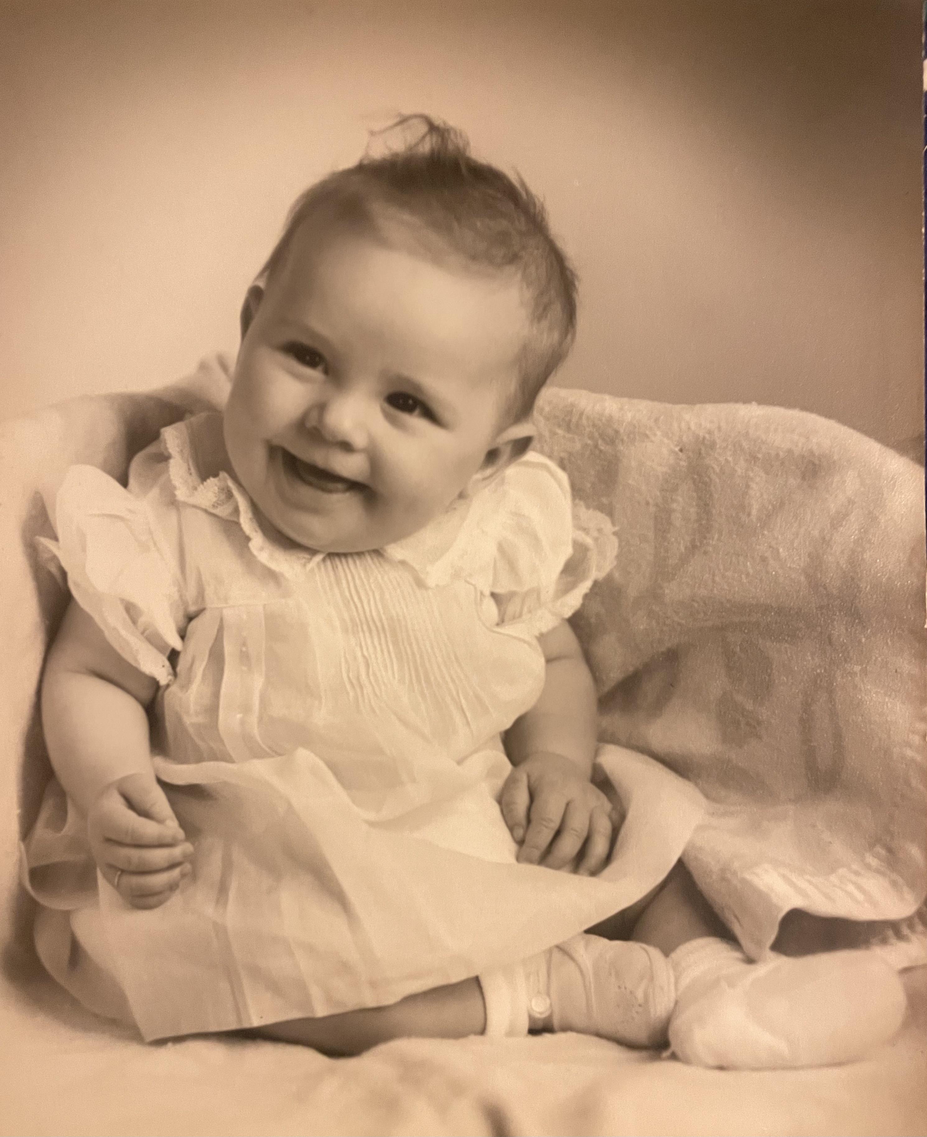 A baby sits in a basket and smiles brightly in a warm, inviting room filled with light.