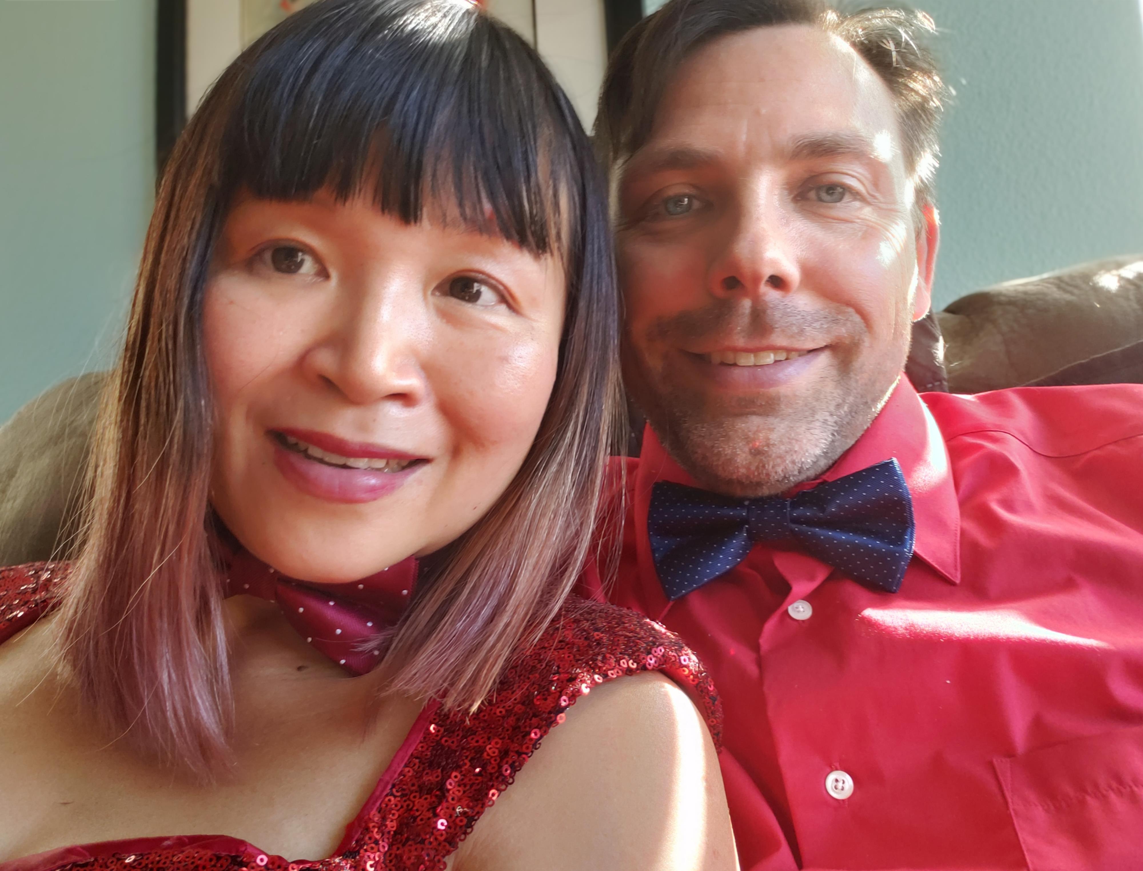 Two people are smiling close together at a gathering. They are dressed in bright clothing.