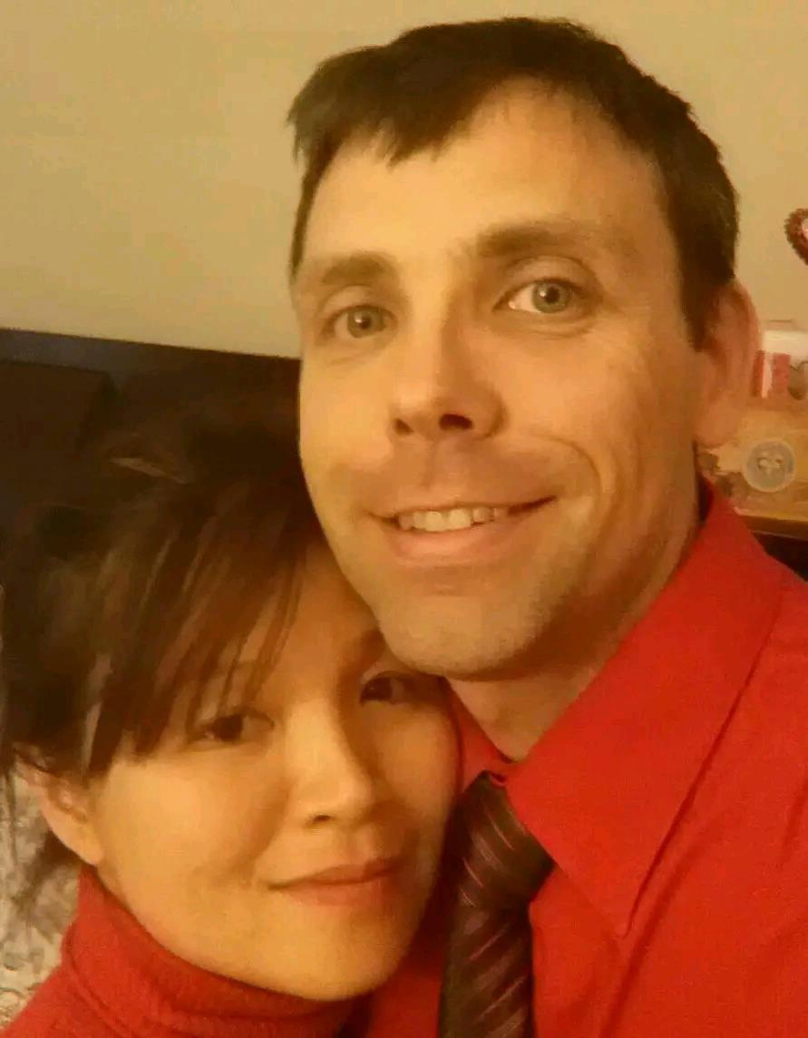 Two people are smiling and posing closely together in a cozy indoor setting.