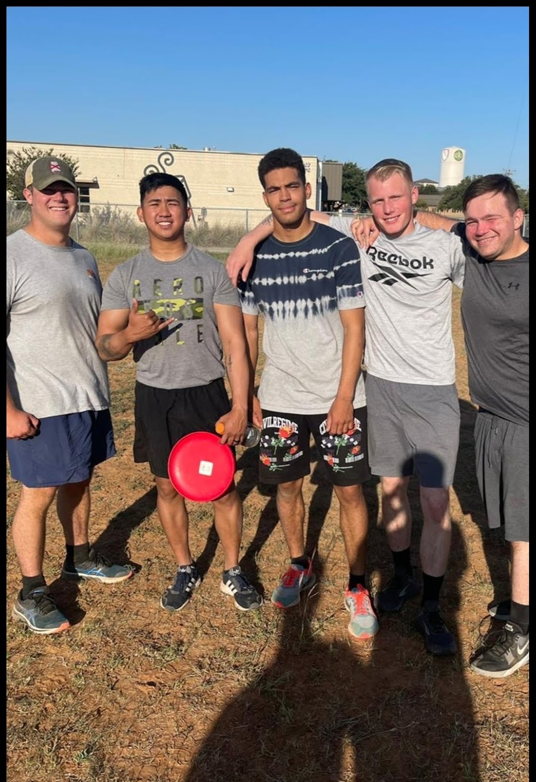 Five friends pose for a picture after playing frisbee on a sports field during the day.