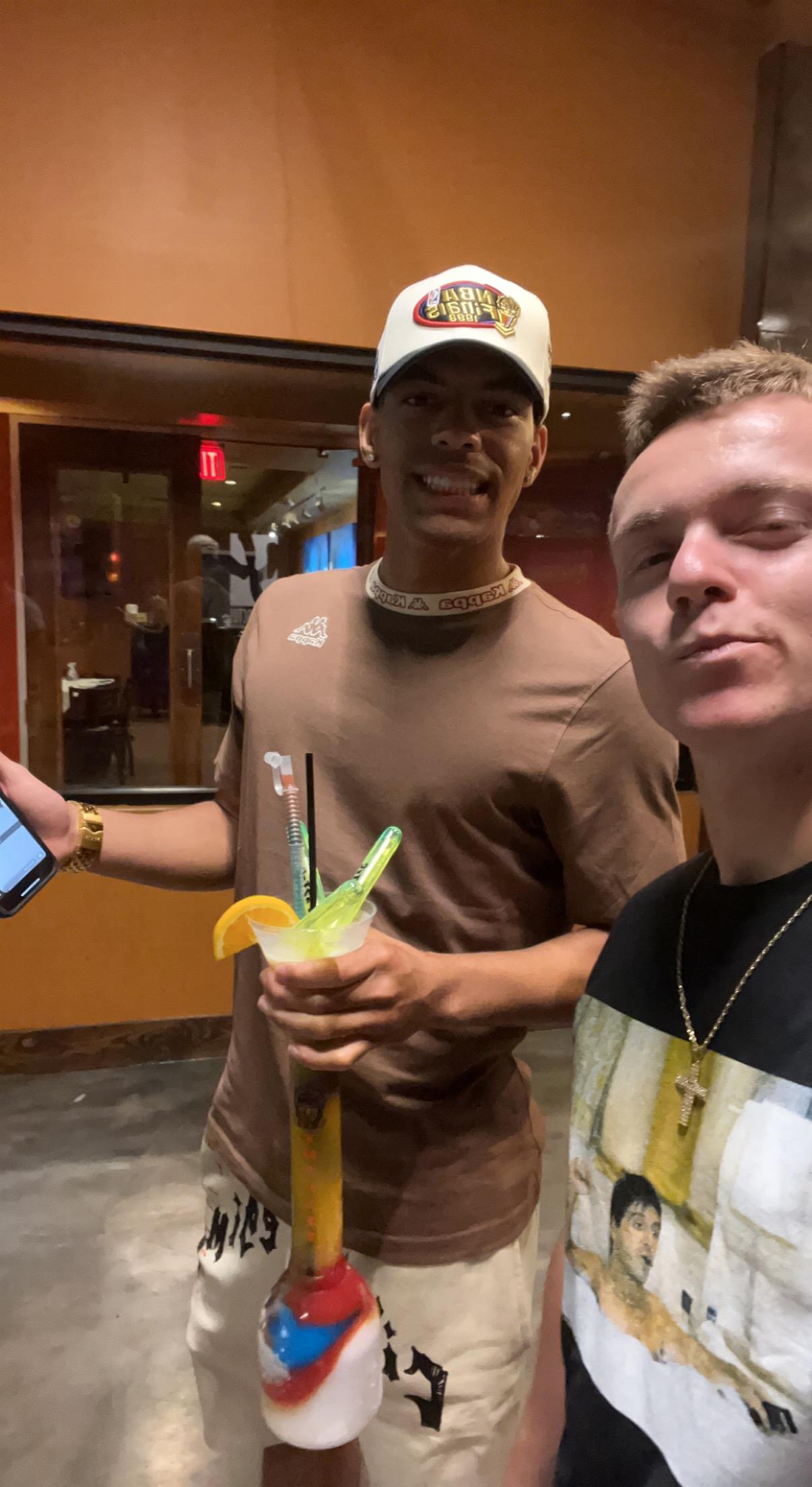 Two men smile and take a selfie while inside a building at night.