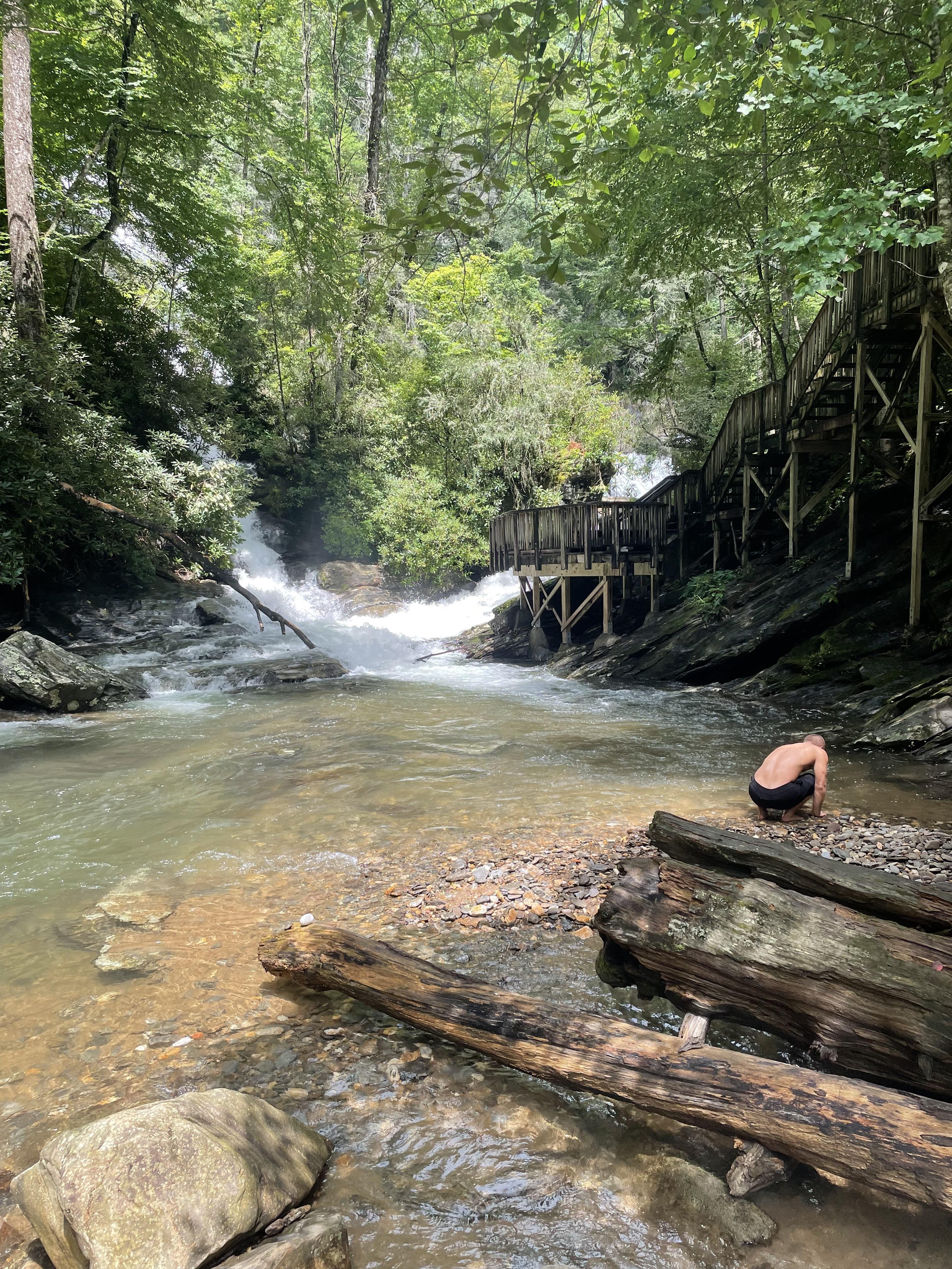 A man in a swimsuit in a river with a wooden bridge