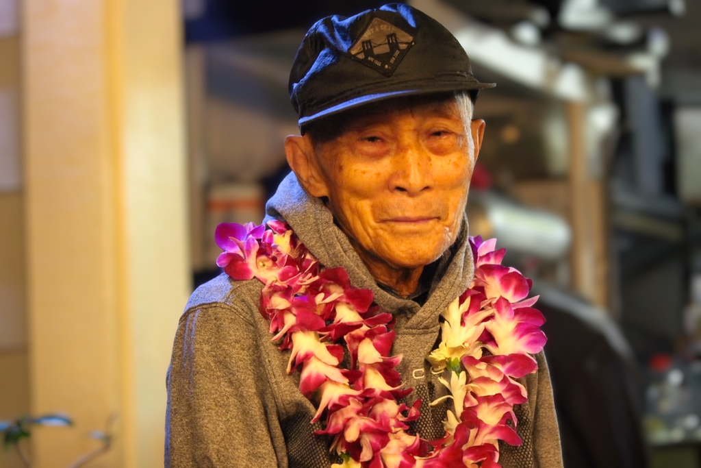 An old man wearing a hat and flower necklace