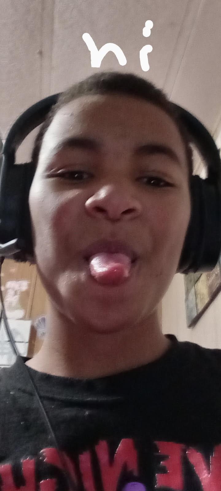 A young boy is smiling and sticking out his tongue while wearing headphones at home.