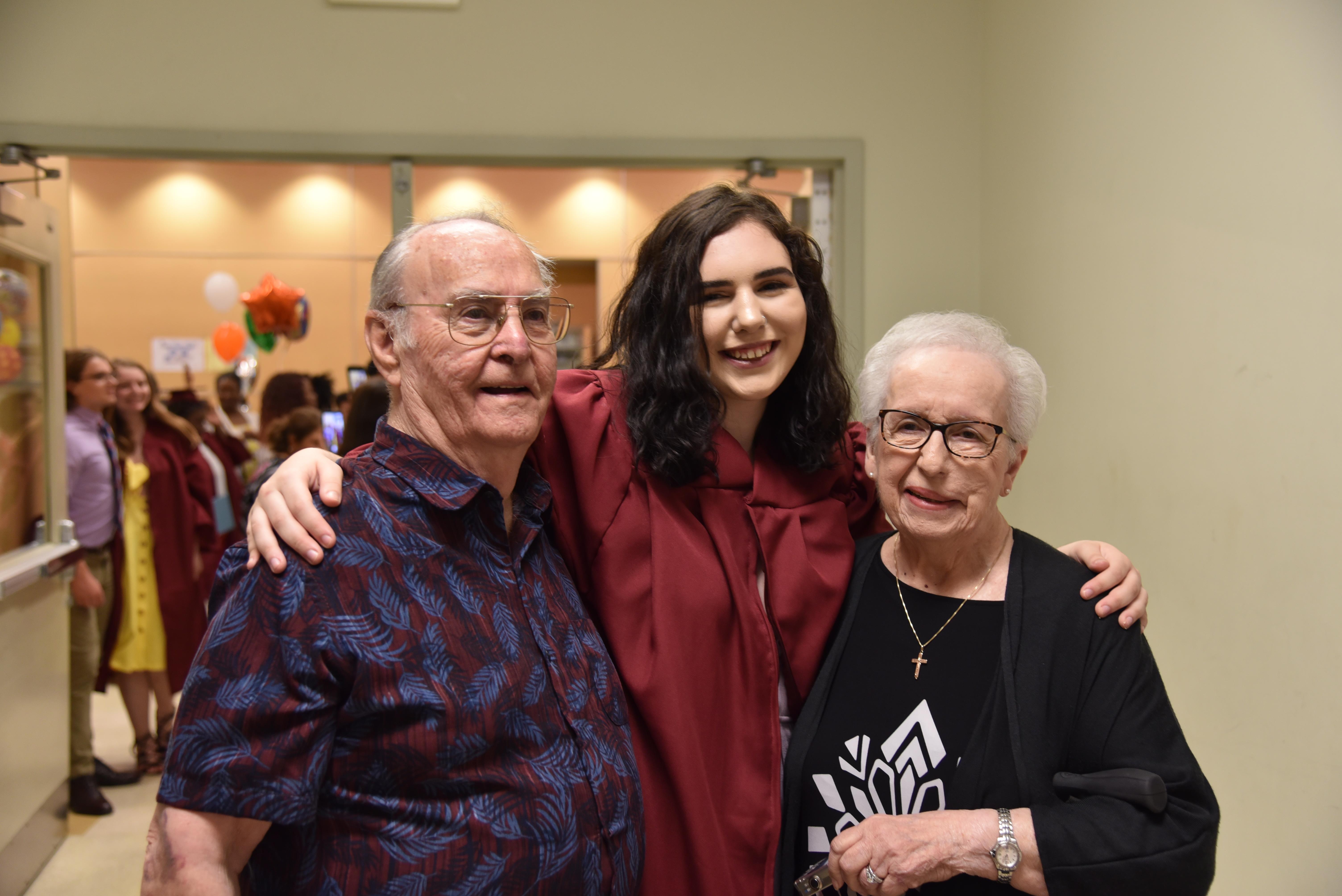 A young woman stands between her grandparents, smiling at a family event in a festive hall.