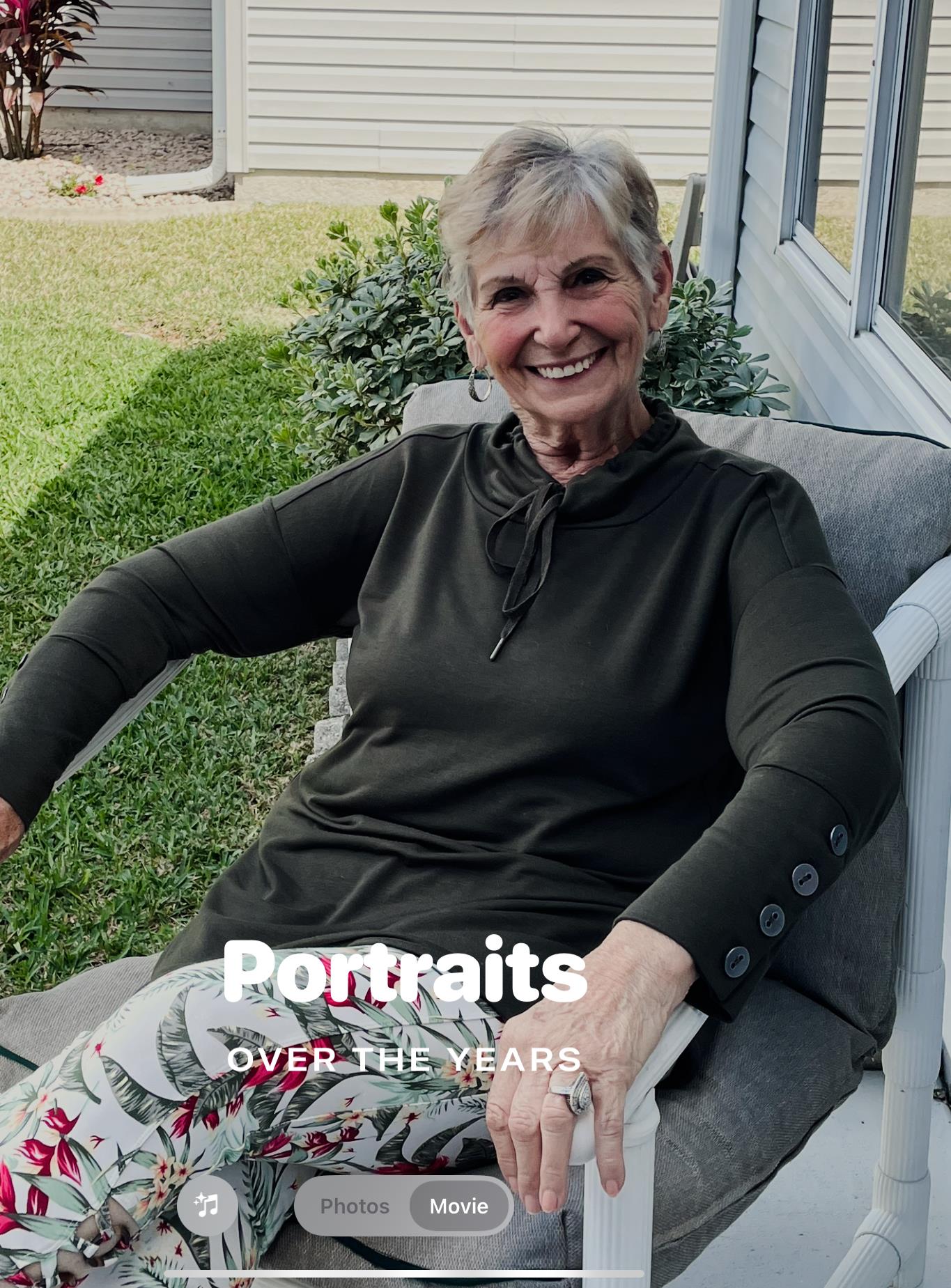 A woman enjoys the warm weather while seated on a chair in her garden, smiling.