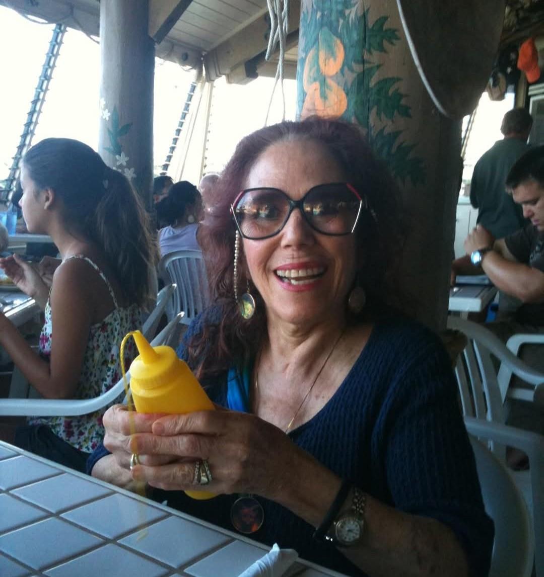 A woman smiles while holding a bottle of mustard in a crowded restaurant near the beach.