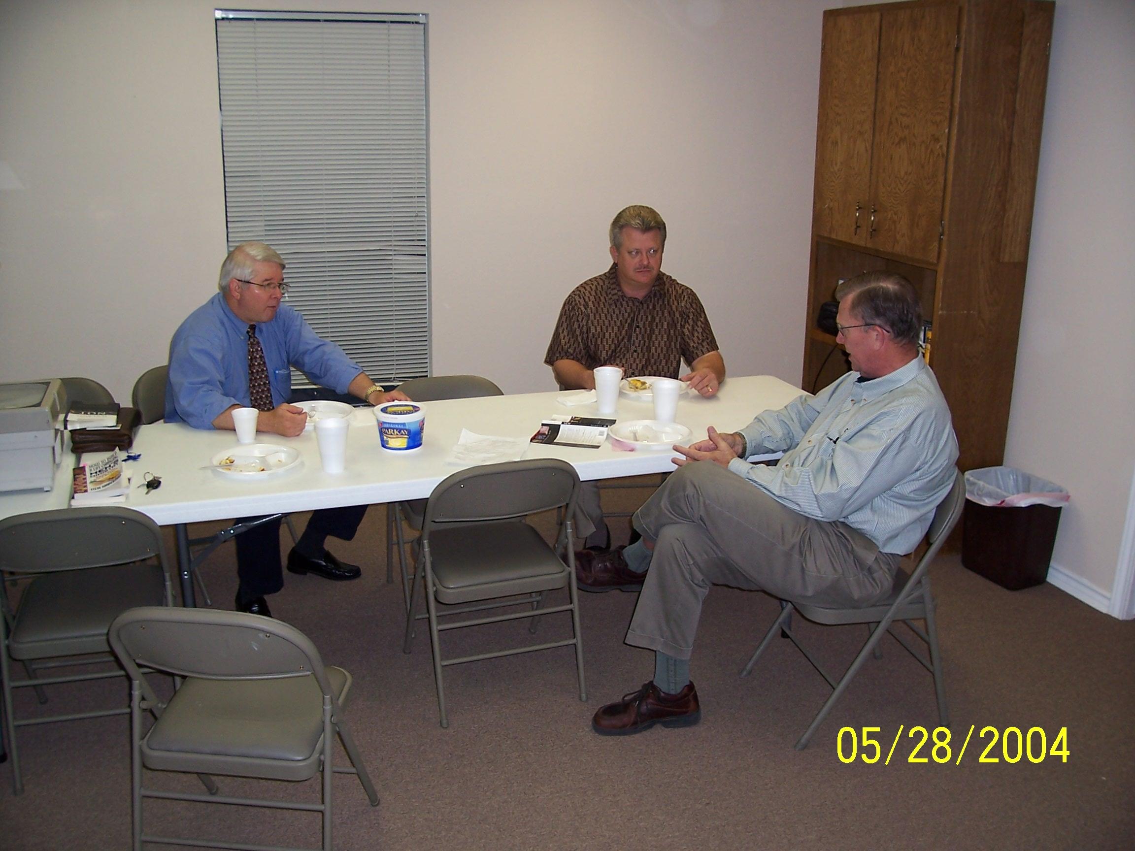 Men sit at a table and talk about work while having snacks during a meeting.