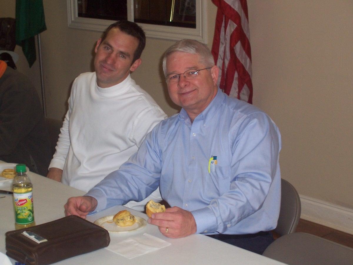 Men are enjoying snacks while seated at a table during a group event in a meeting space.