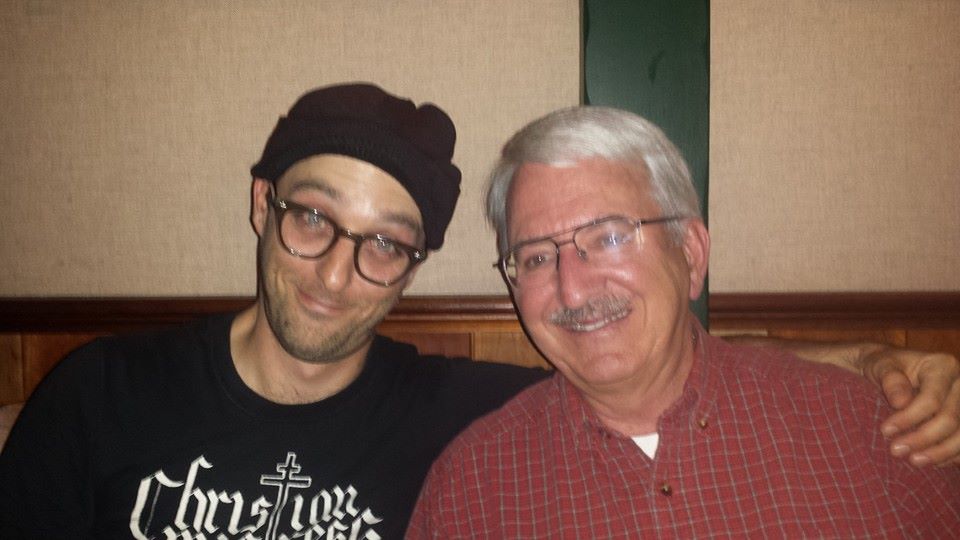 Two men sit next to each other, both smiling, at a restaurant during a friendly meeting.