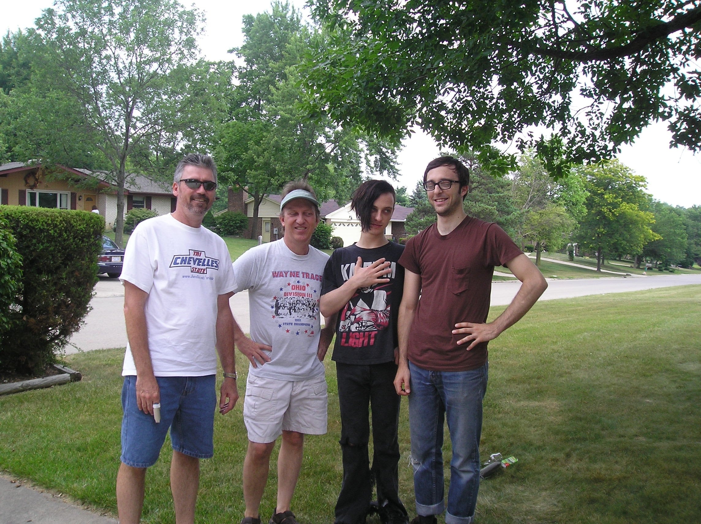 Four men are standing on the sidewalk near some houses.