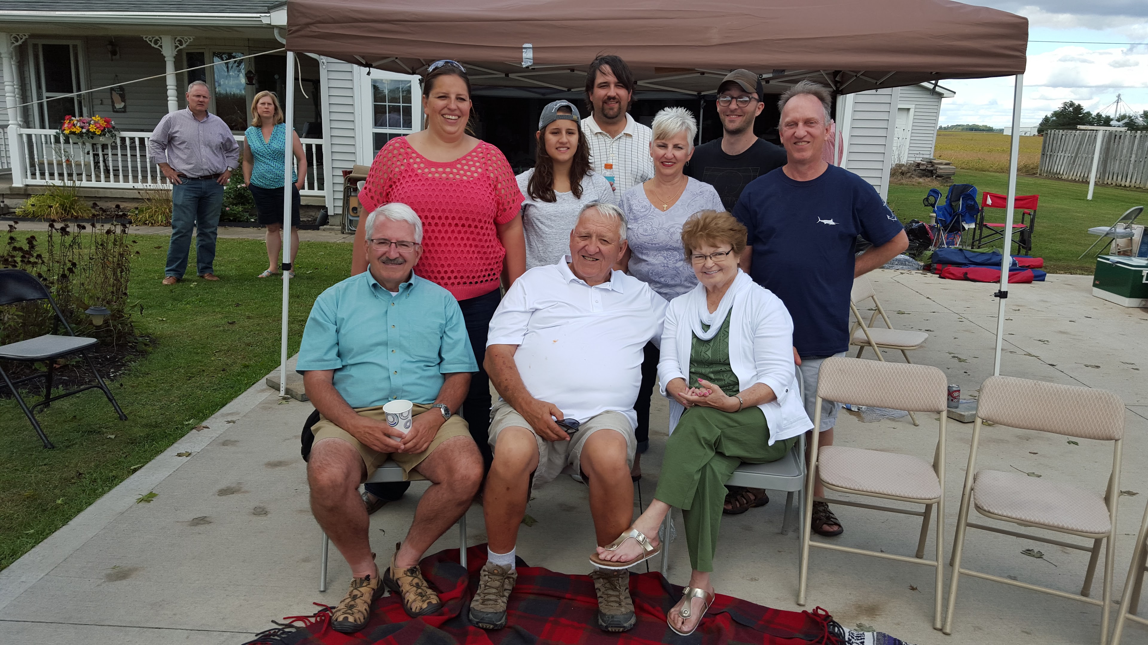 A group of people poses together in a backyard during a warm day for a social gathering.