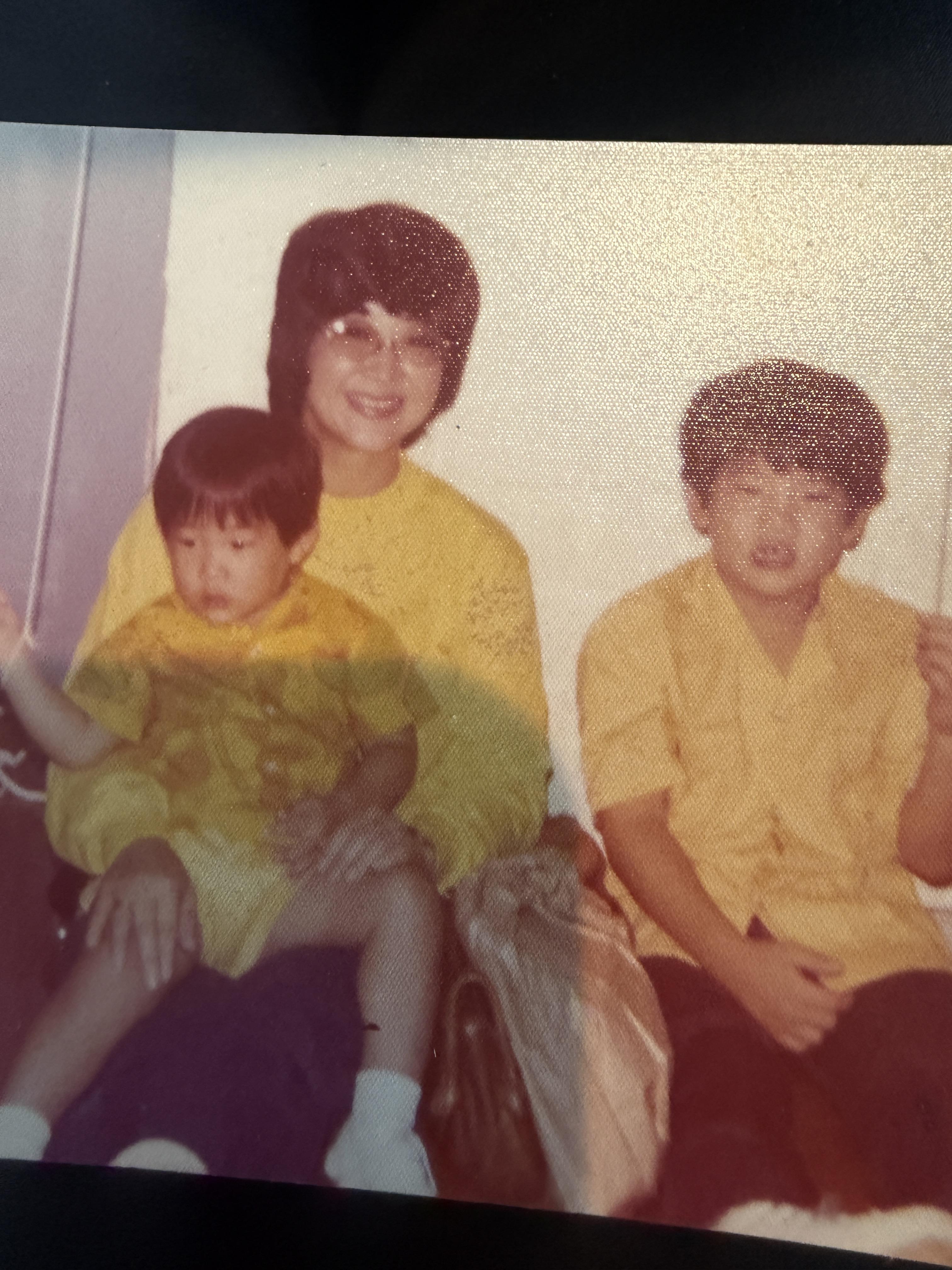 A woman and two kids in matching yellow shirts smile together indoors.
