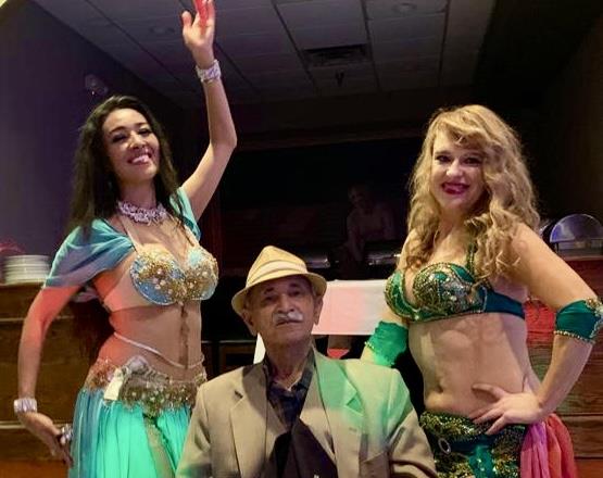 Two dancers entertain a crowd at a cultural event while sitting man watches and smiles.