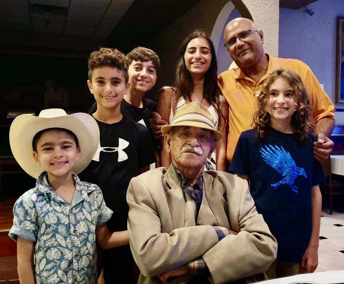 Family members smile and pose together during a gathering. There are seven people in the group.