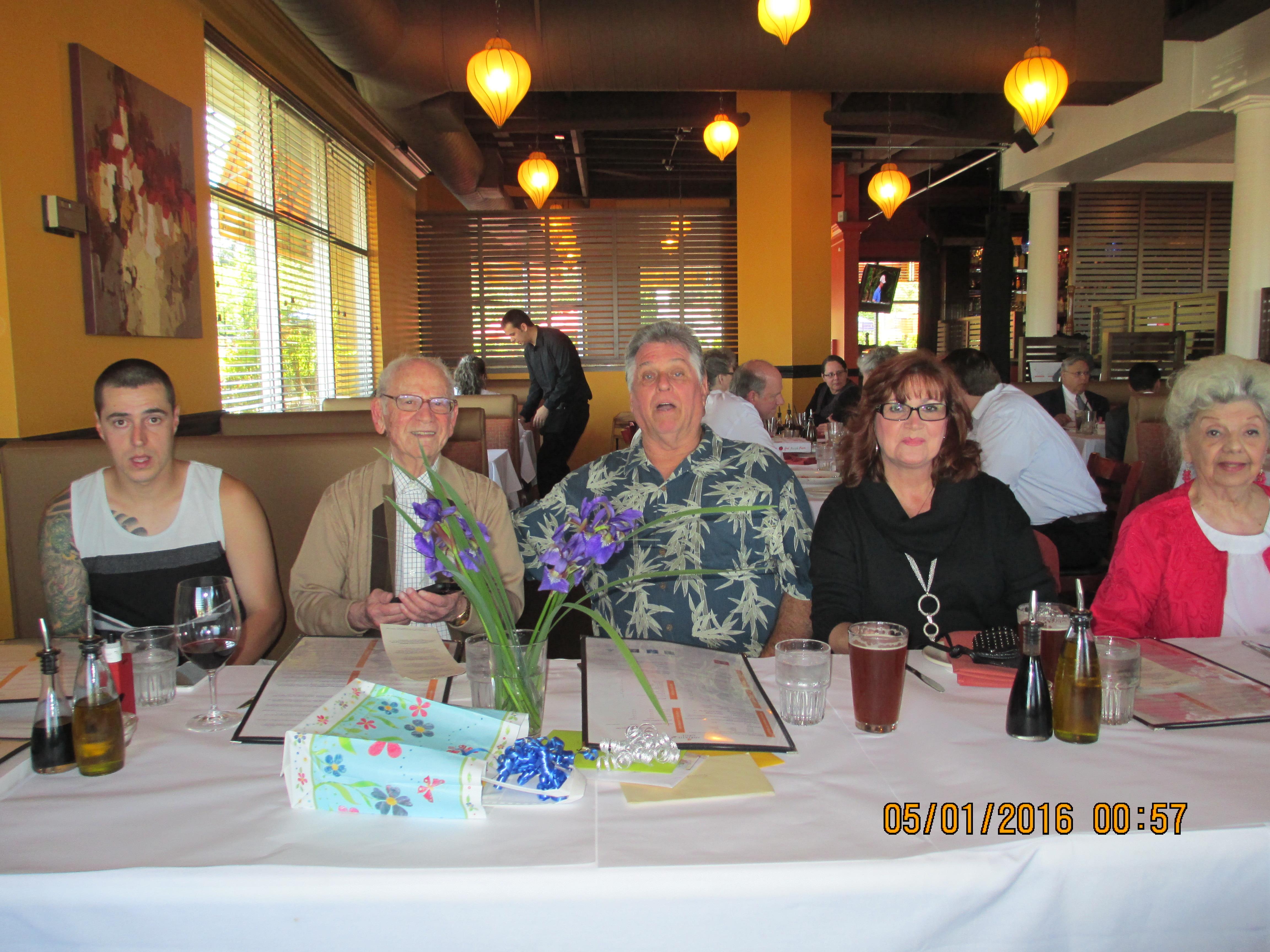 Four individuals sit at a table with menus in a restaurant at lunchtime with people around.
