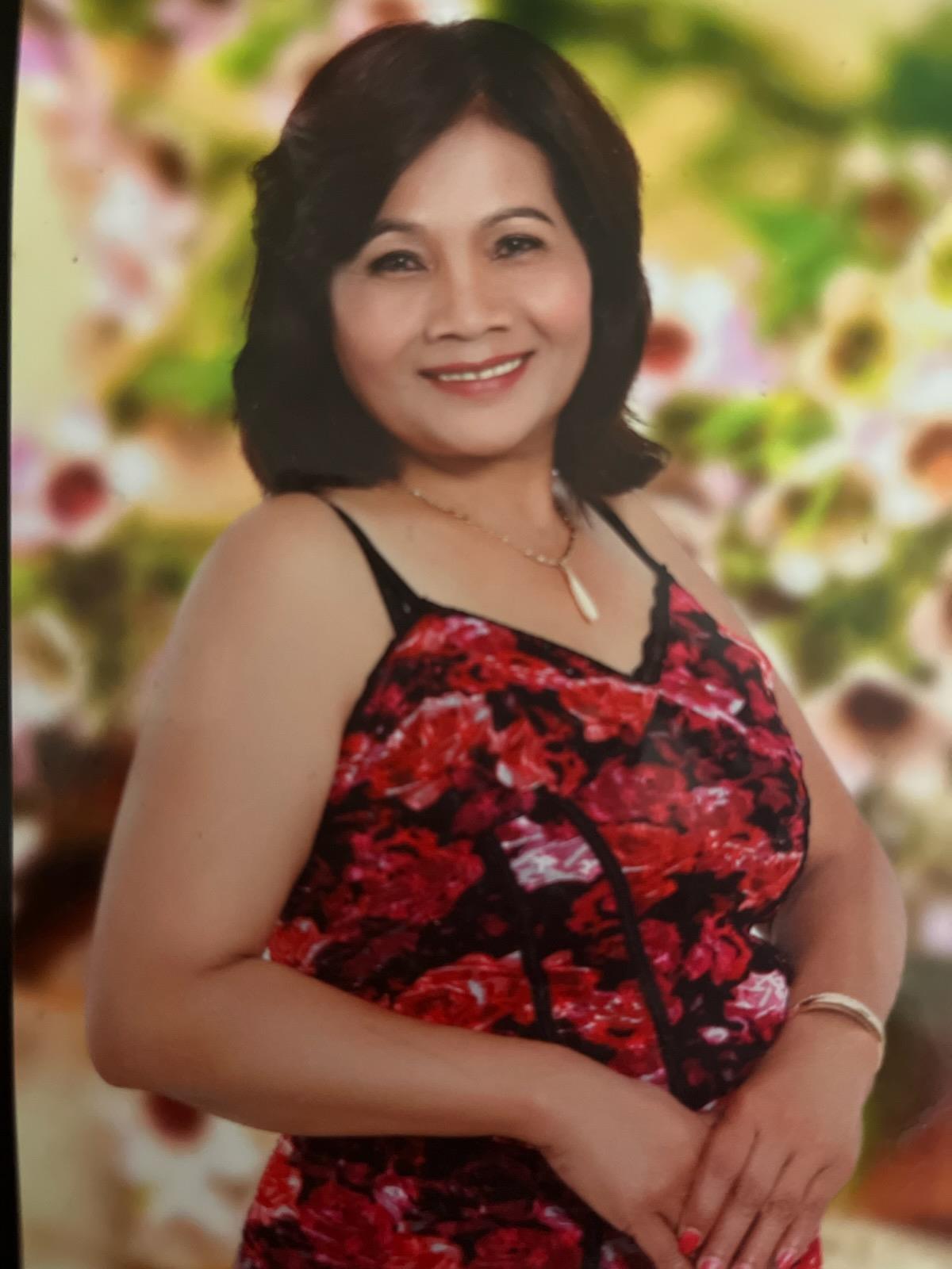 A woman stands with a smile in a red floral top in front of a bright background.