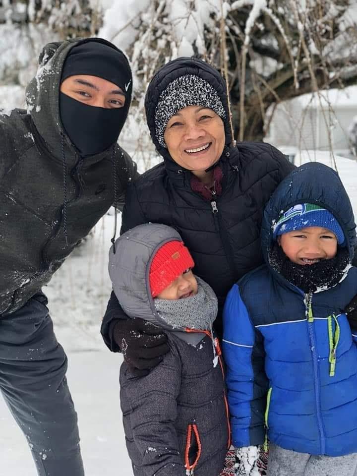 Four people stand together in the snow, smiling and bundled up for winter. They appear happy.