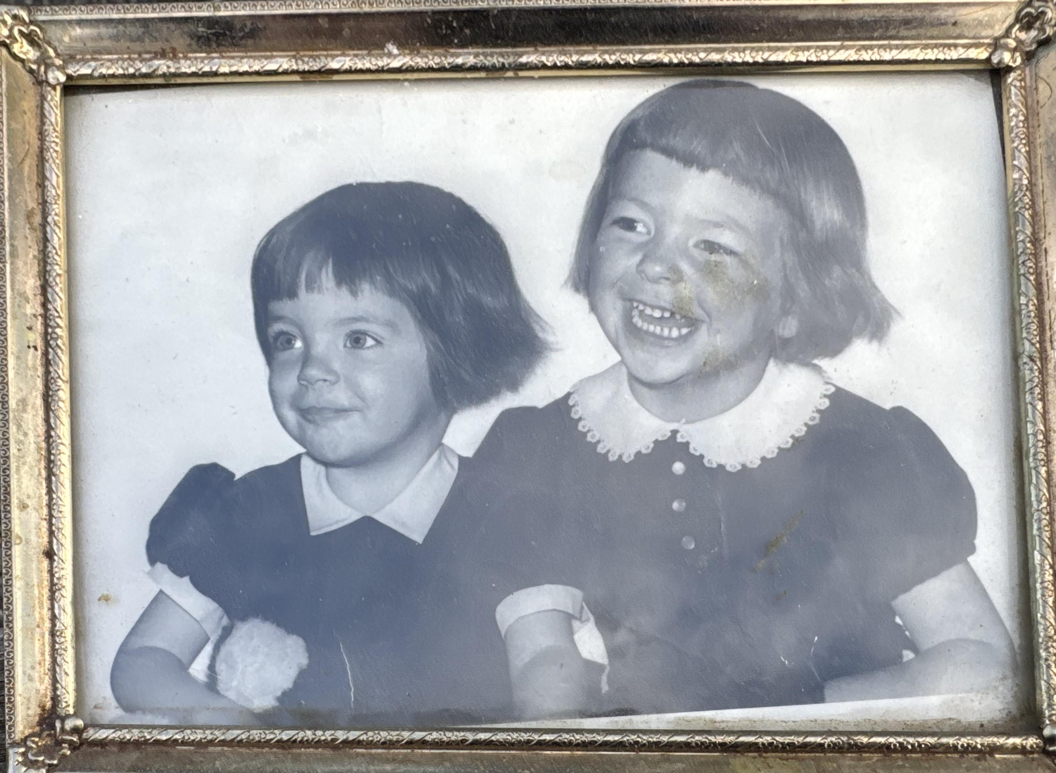 Two girls sit close to each other and smile. They appear happy and engaged in a moment together.